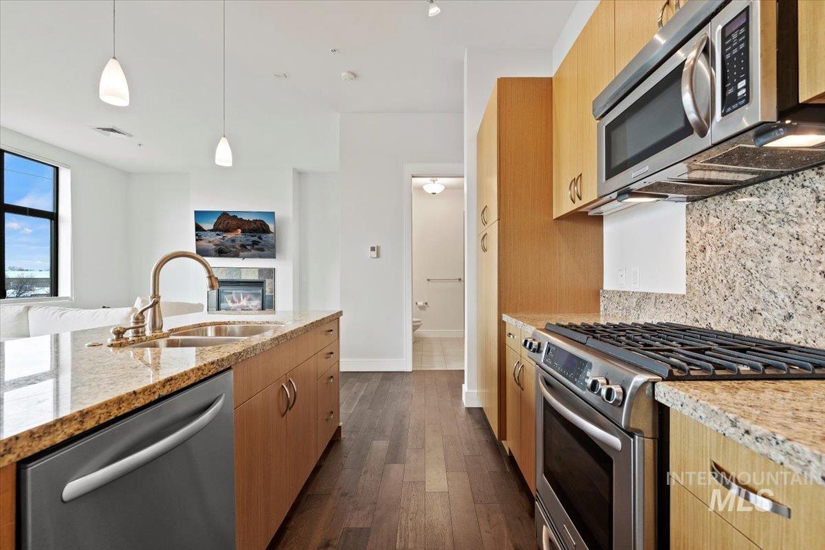 Kitchen featuring appliances with stainless steel finishes, light stone countertops, decorative light fixtures, dark wood-style floors, and light brown cabinetry