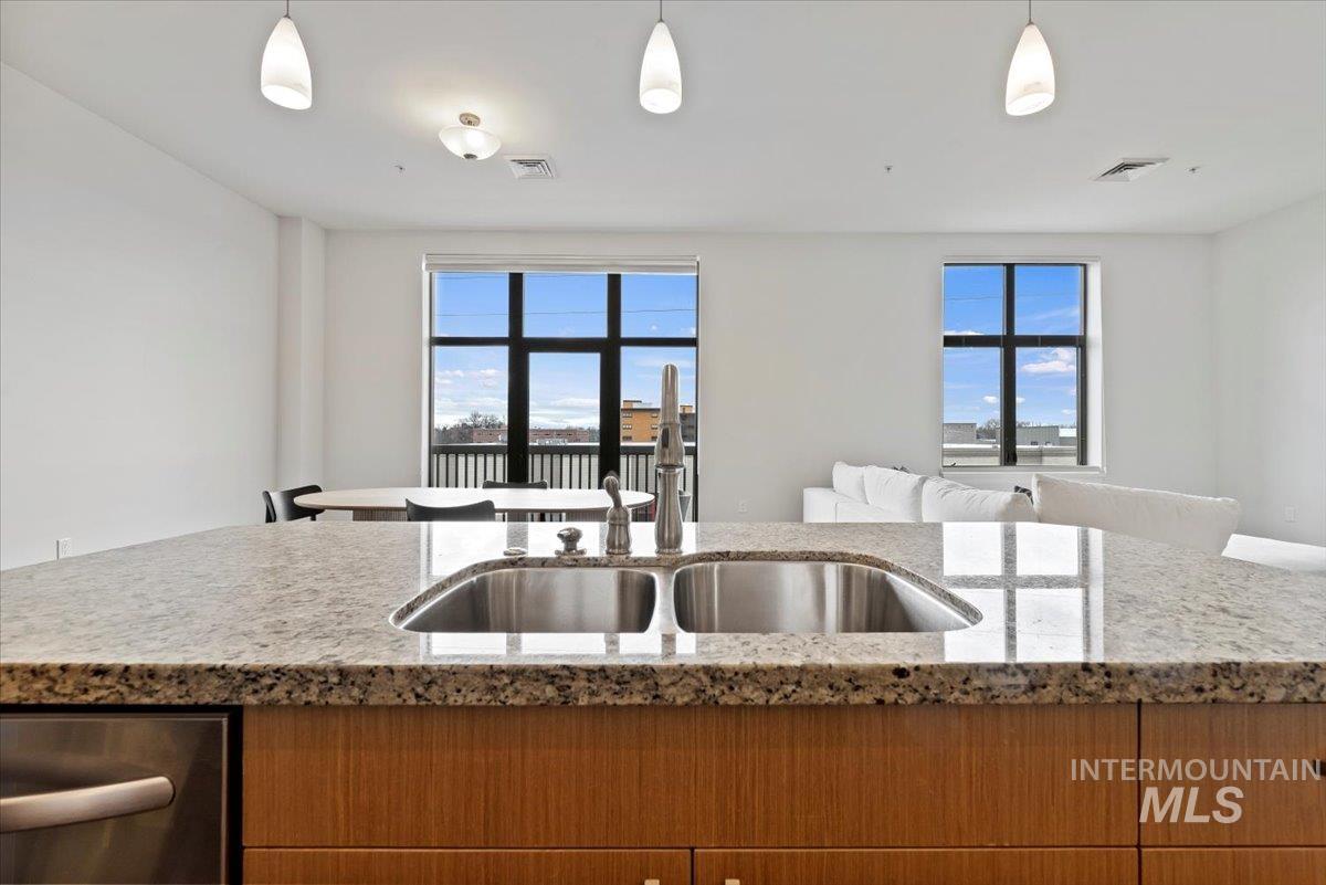 Kitchen with light stone countertops, open floor plan, dishwasher, hanging light fixtures, and plenty of natural light