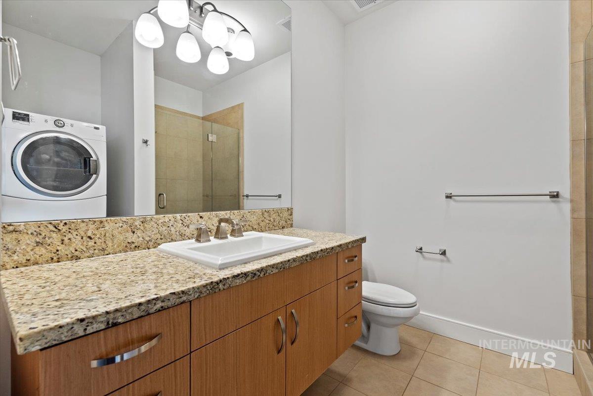 Full bath with washer / clothes dryer, vanity, a stall shower, and light tile patterned floors