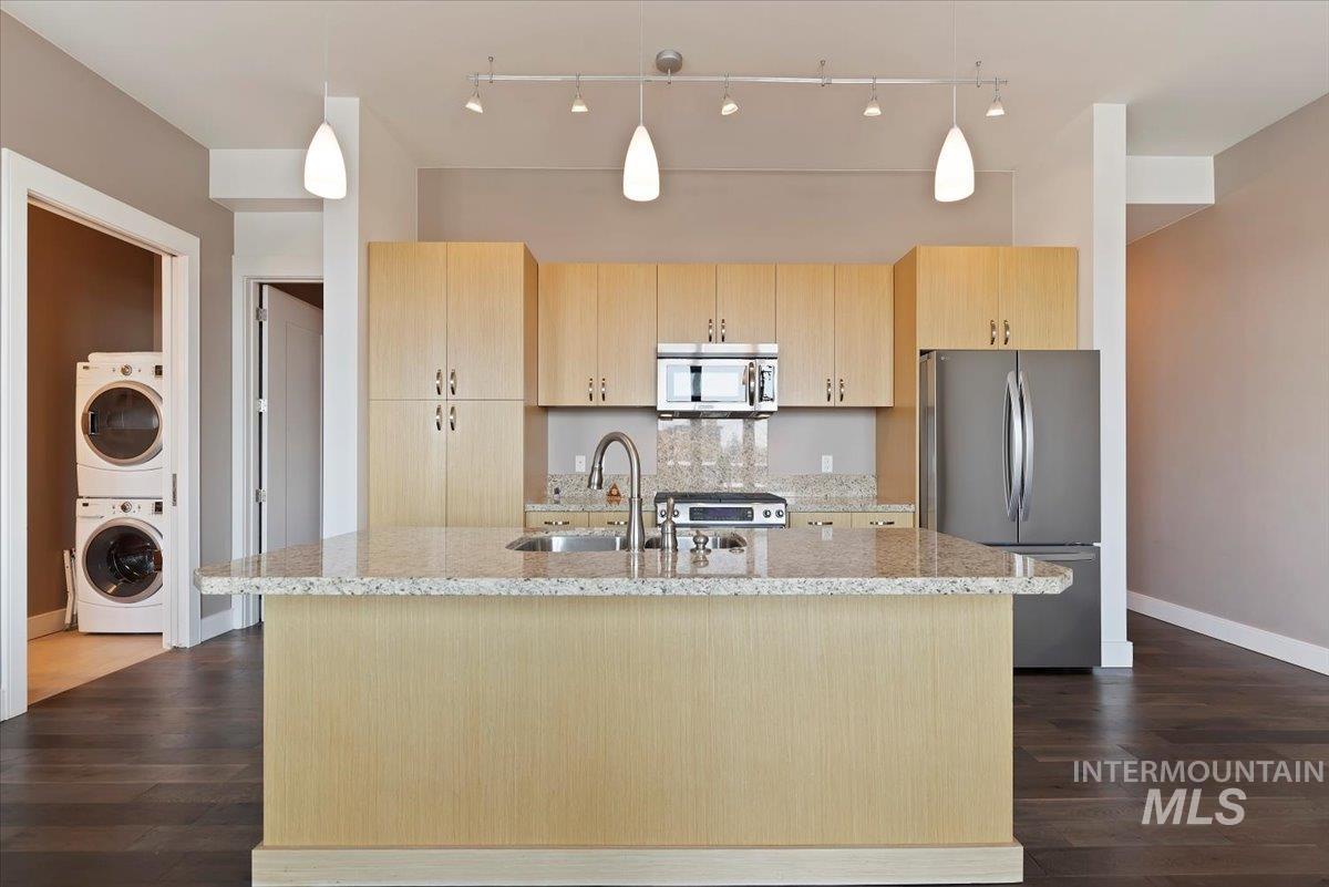 Kitchen featuring light brown cabinetry, stainless steel appliances, light stone countertops, and dark wood-type flooring