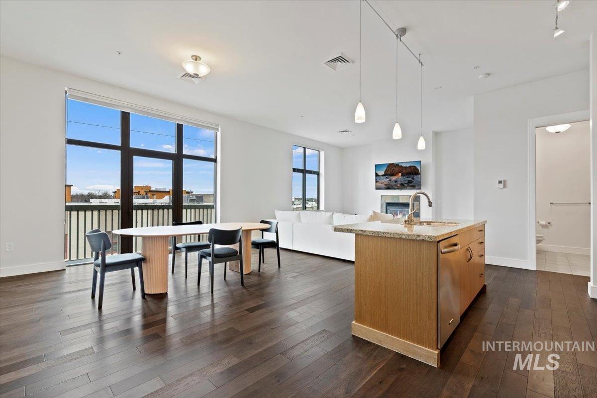 Kitchen featuring a center island with sink, hanging light fixtures, light stone counters, open floor plan, and dark wood finished floors