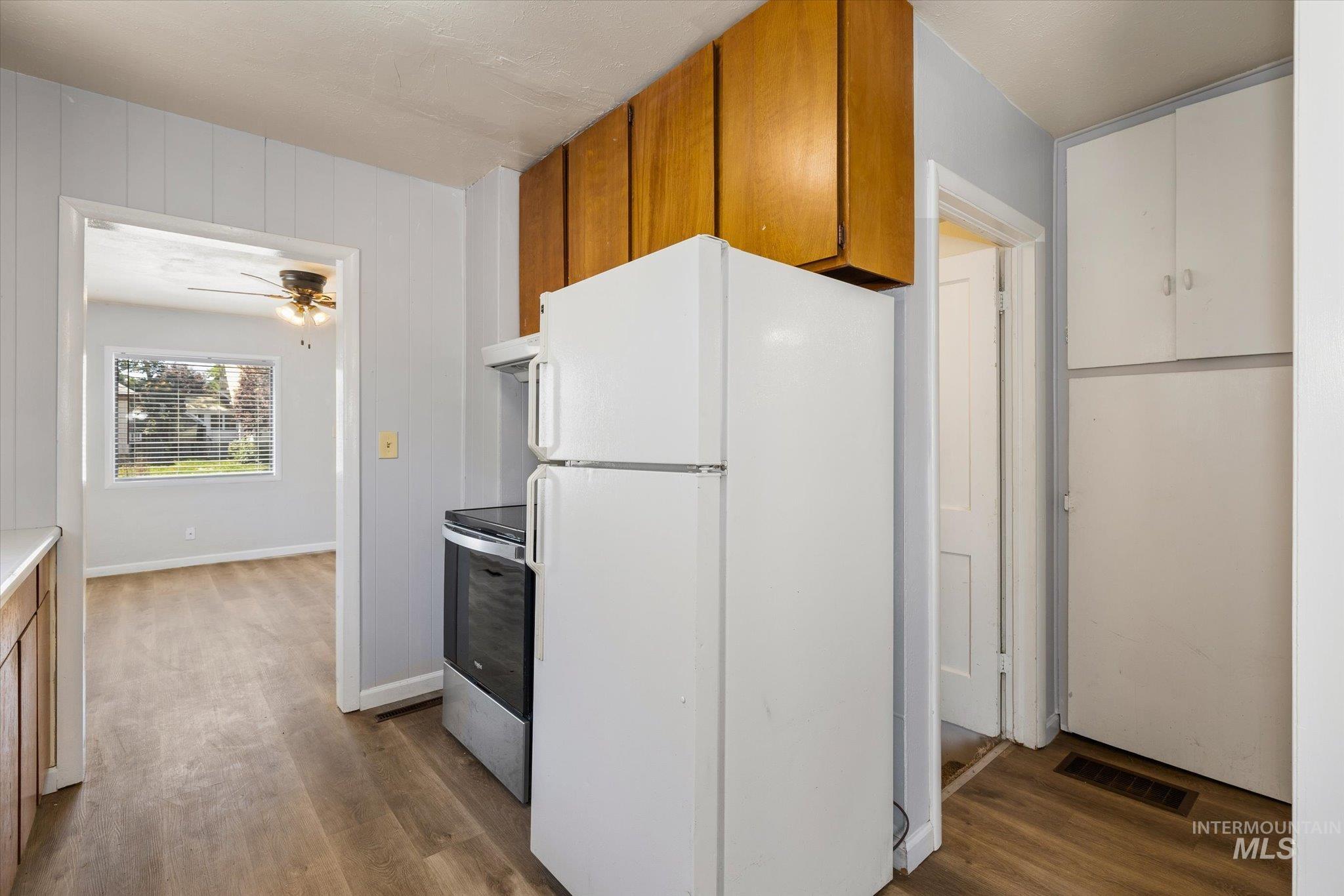 Kitchen area featuring wood-finish flooring, white paneled walls, and wood cabinetry