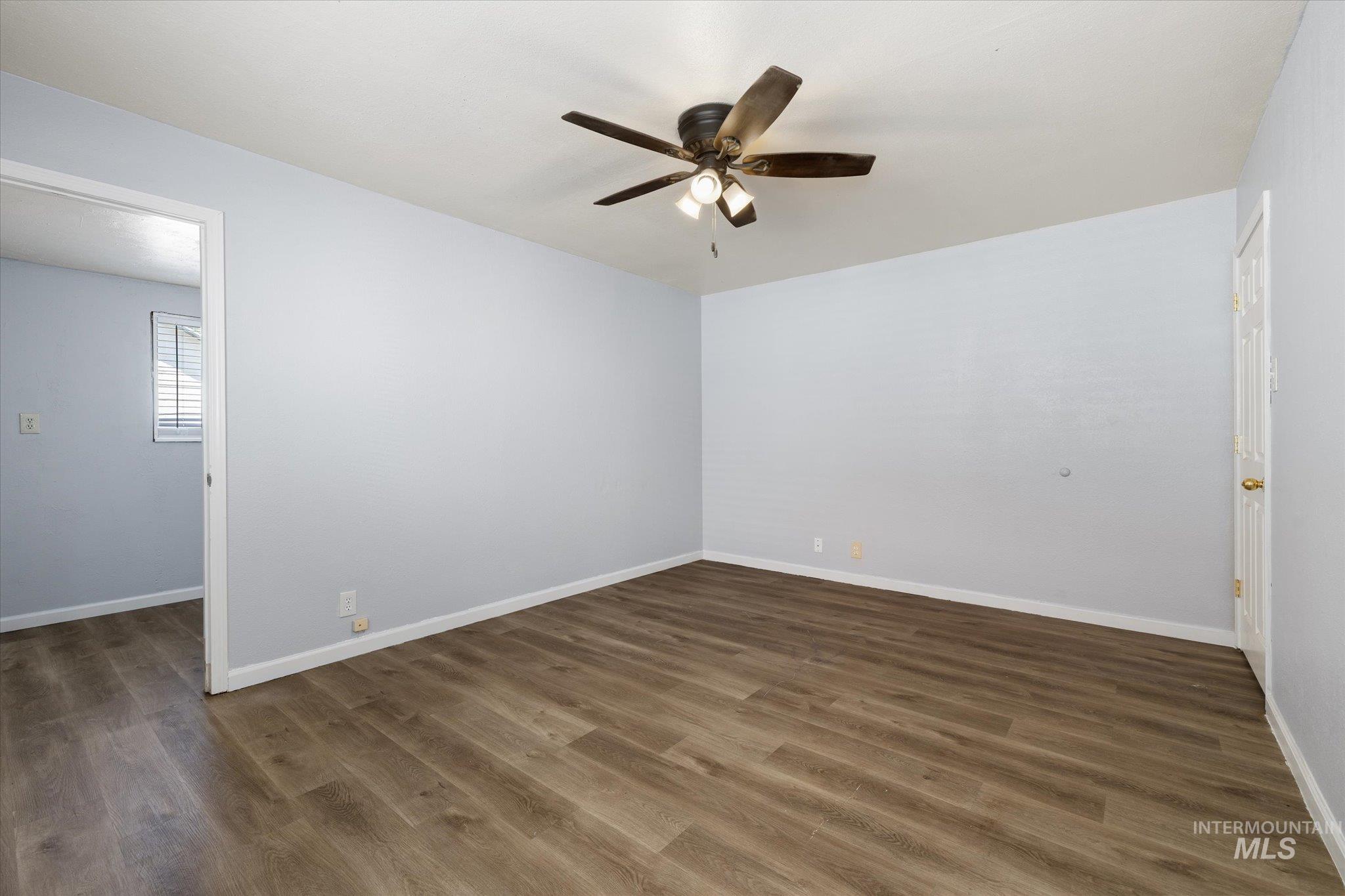 Spacious room featuring wood-finish flooring, light blue walls, and a ceiling fan with integrated lighting
