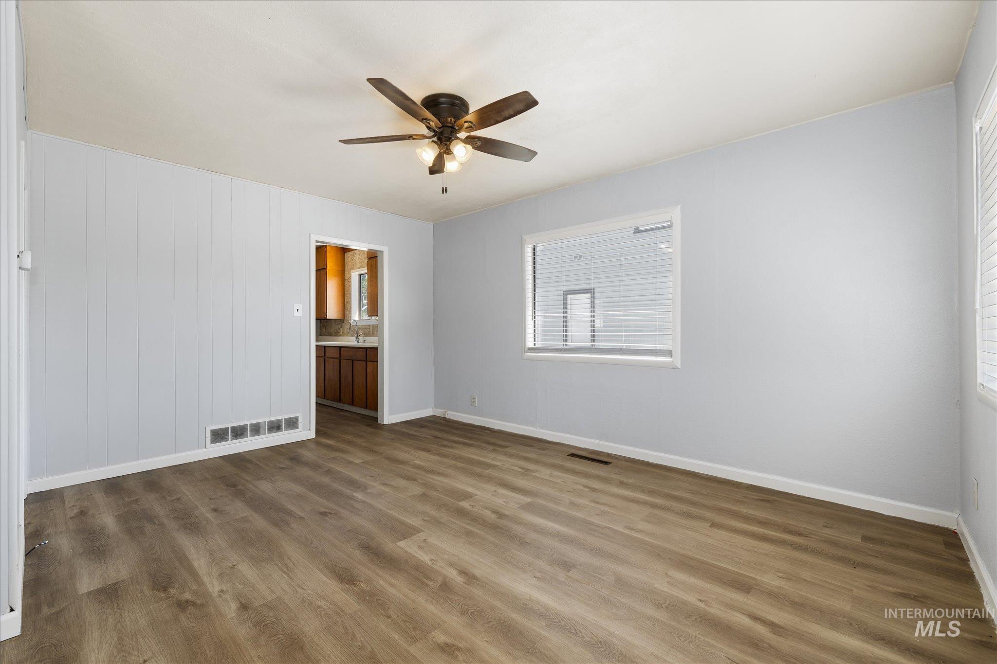 Spacious room featuring wood-finish flooring, light blue walls, and a ceiling fan with integrated lighting