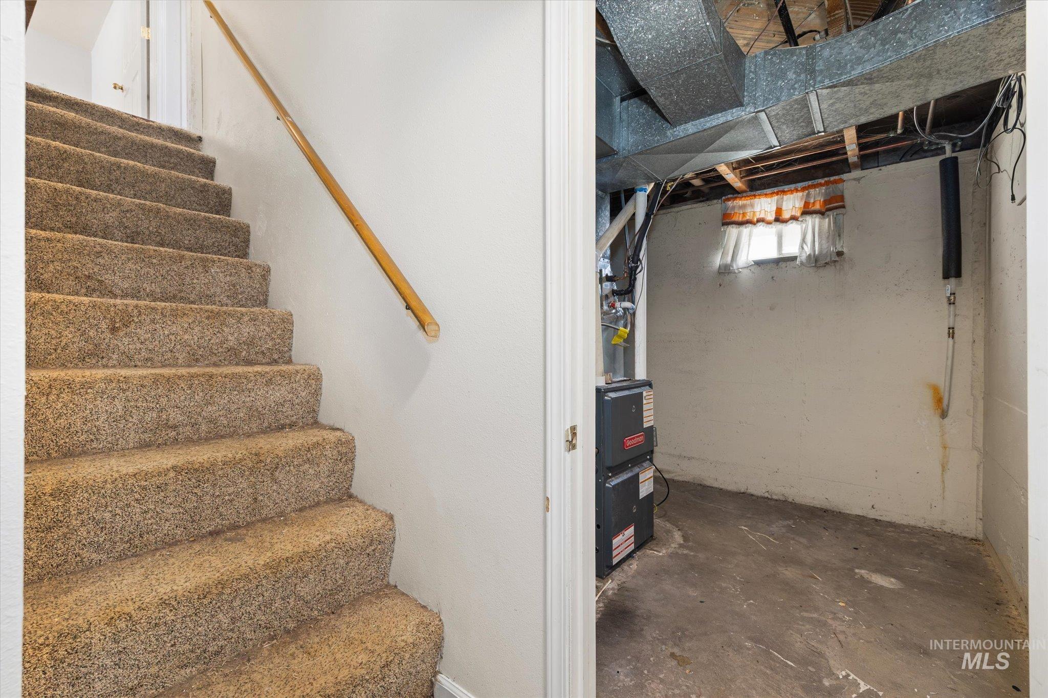 Carpeted staircase with wood handrail, leading to a utility area featuring exposed ductwork, a furnace, and a small window