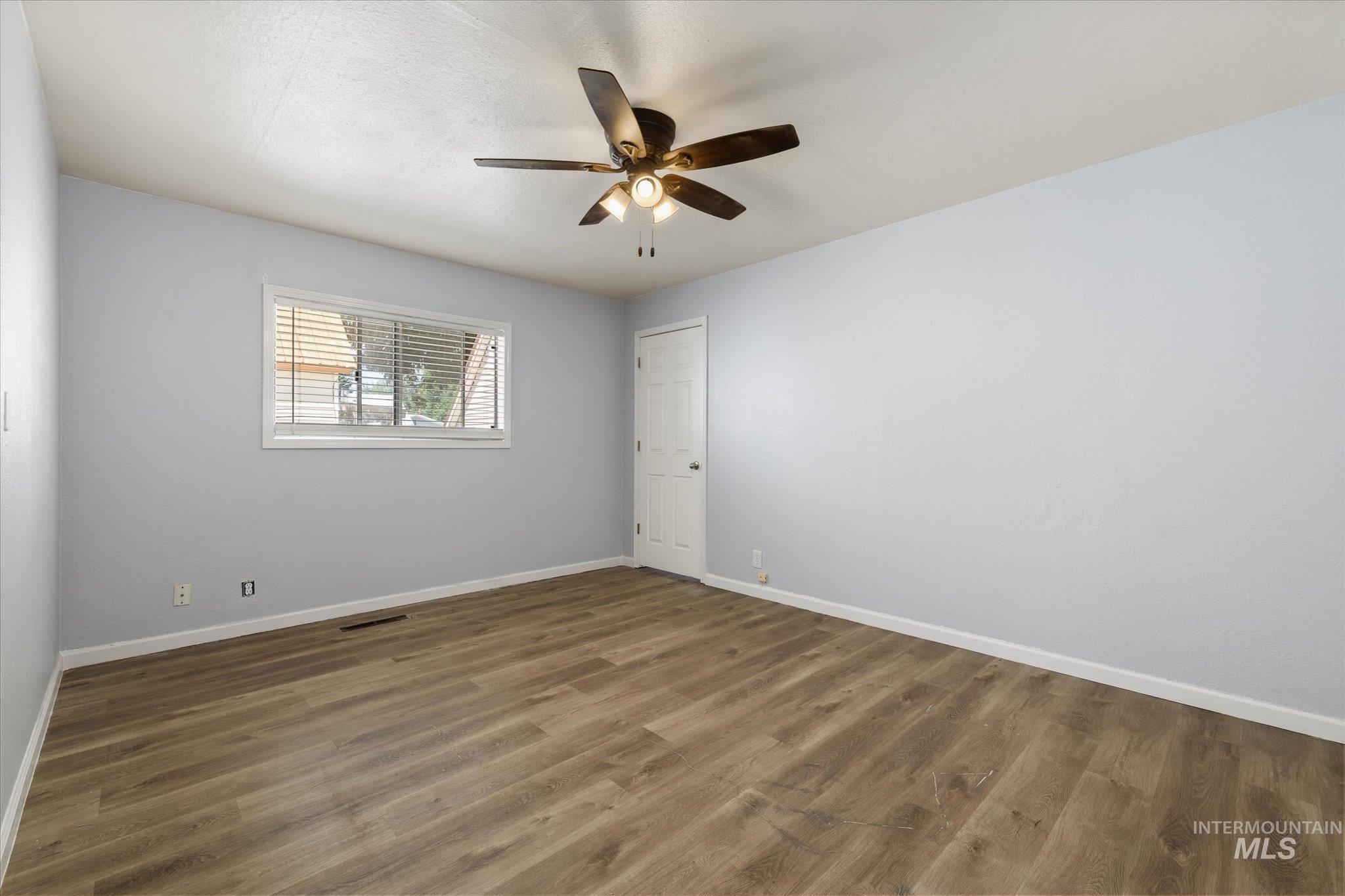 Spacious room featuring wood-finish flooring, light gray walls, white trim, and a ceiling fan with integrated lighting