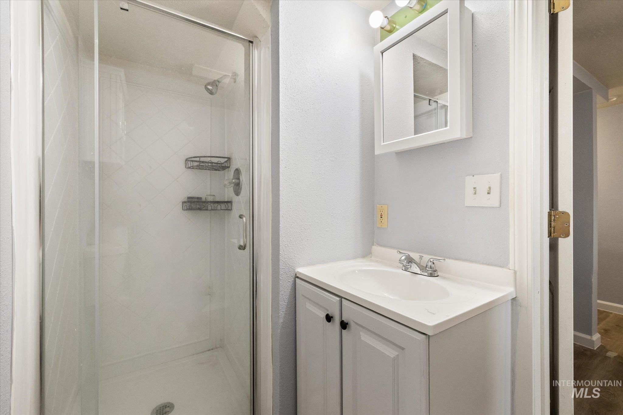 Bathroom featuring a glass-enclosed shower with tiled walls, a white vanity with an integrated sink, and a wall-mounted medicine cabinet with an attached light fixture
