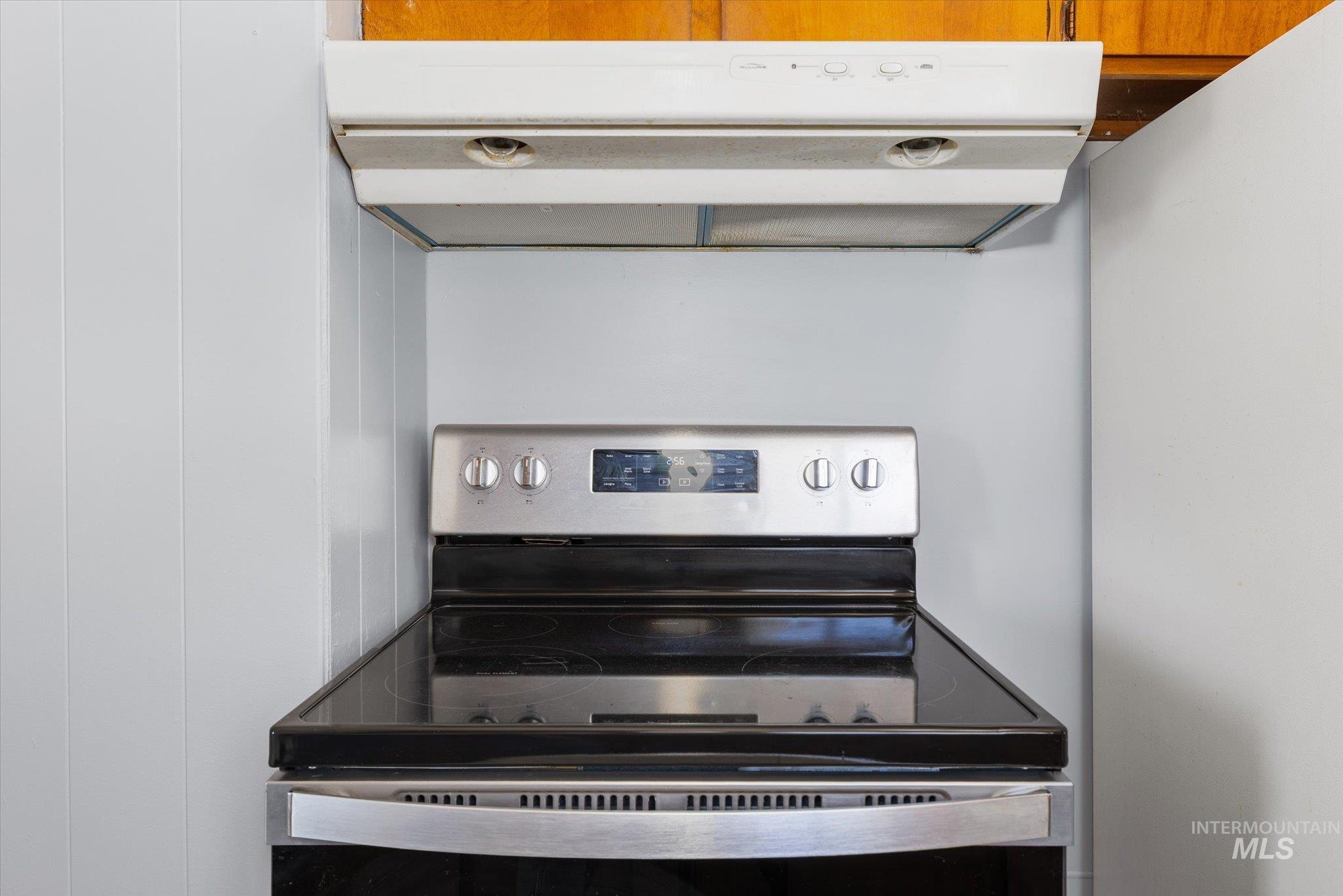 Stainless steel electric range with a black ceramic cooktop, complemented by a white overhead range hood
