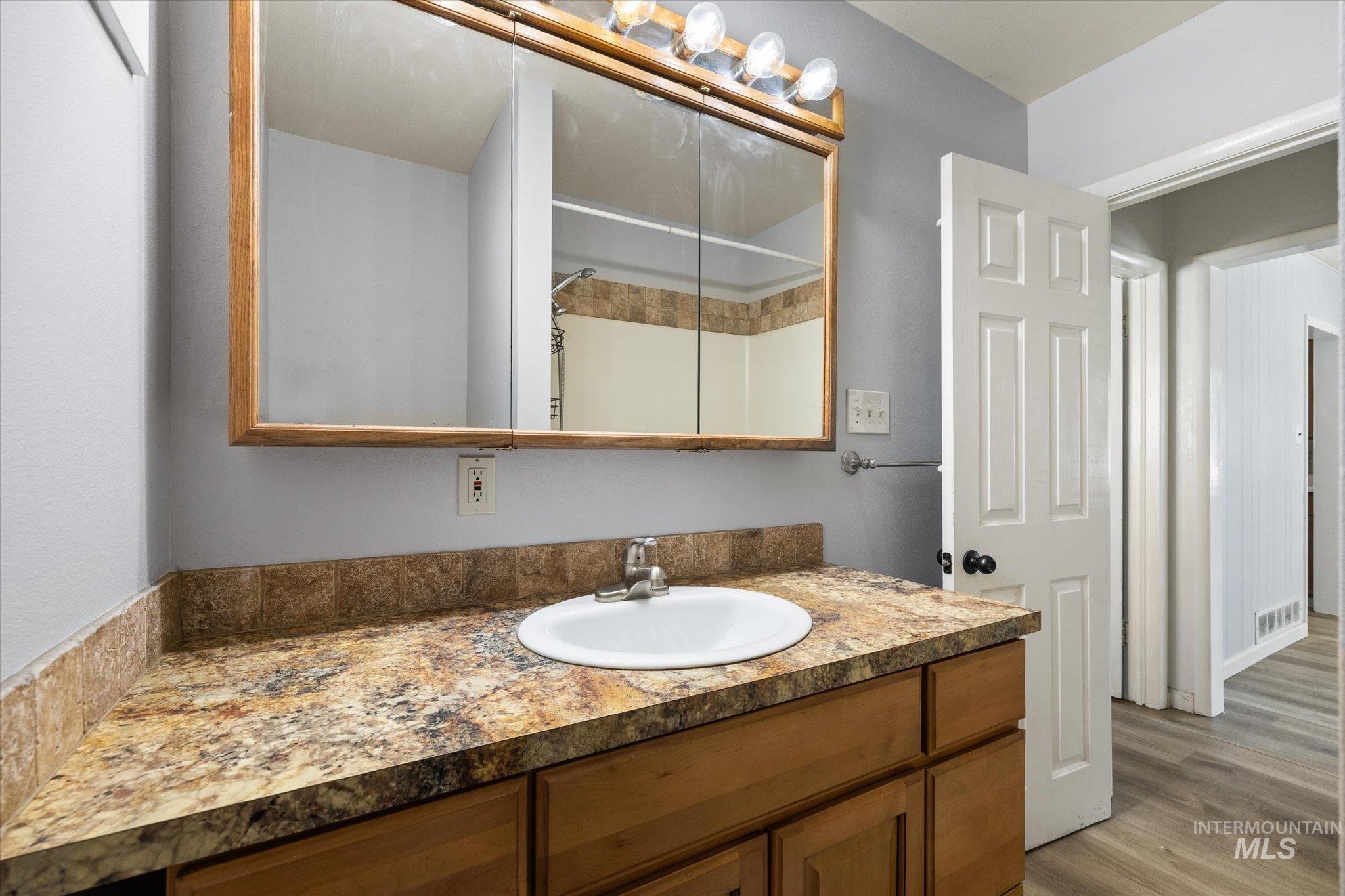 Bathroom vanity featuring a built-in sink, wood-finish cabinetry, and a patterned countertop with a matching backsplash