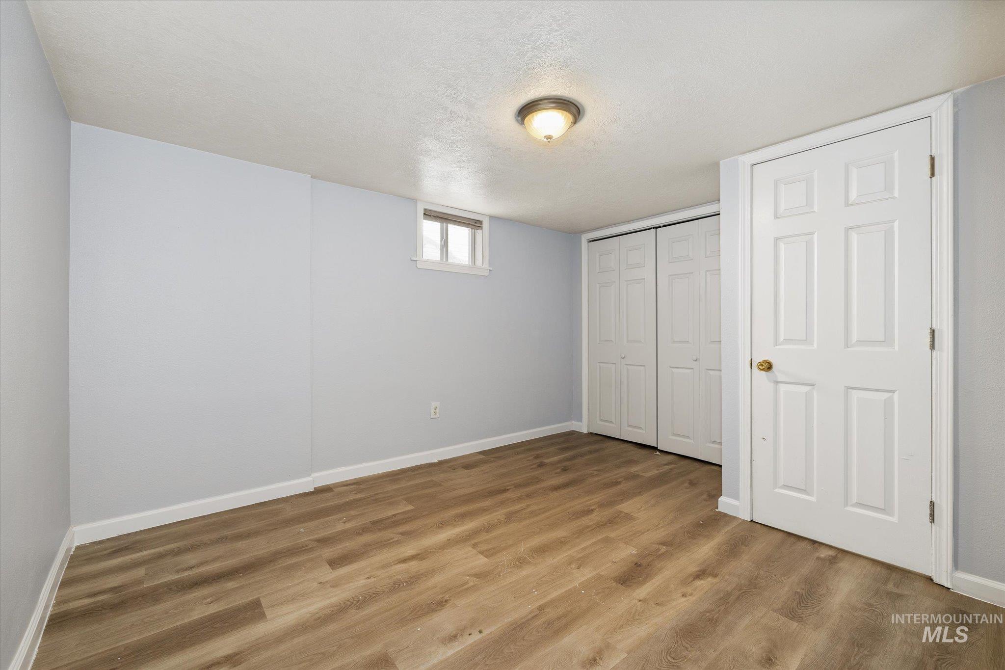 Room featuring wood-finish flooring, two bi-fold closet doors, a single window, and a flush mount ceiling light fixture