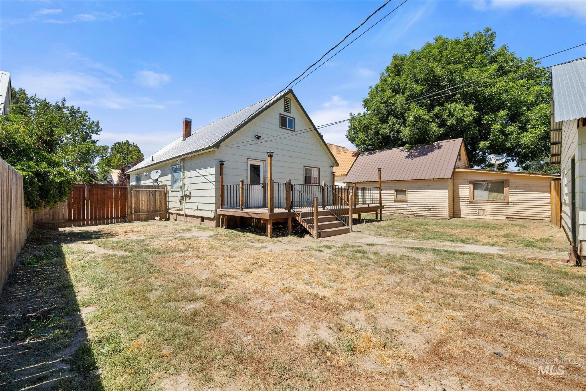 Rear exterior featuring a wooden deck with railing and stairs, a separate auxiliary structure with a metal roof, and perimeter wood fencing