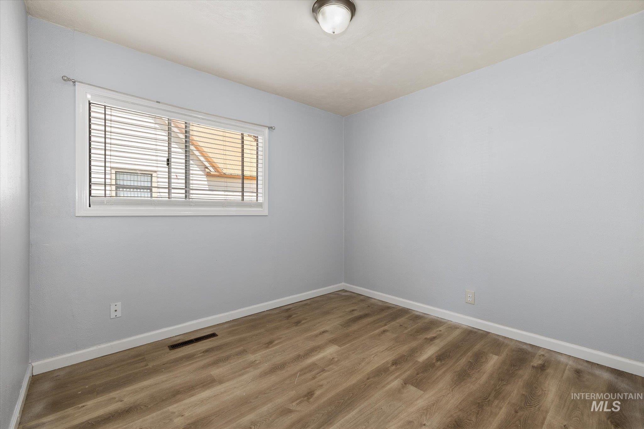 Room featuring light blue walls, wood-finish flooring, white baseboards, and a window with horizontal blinds