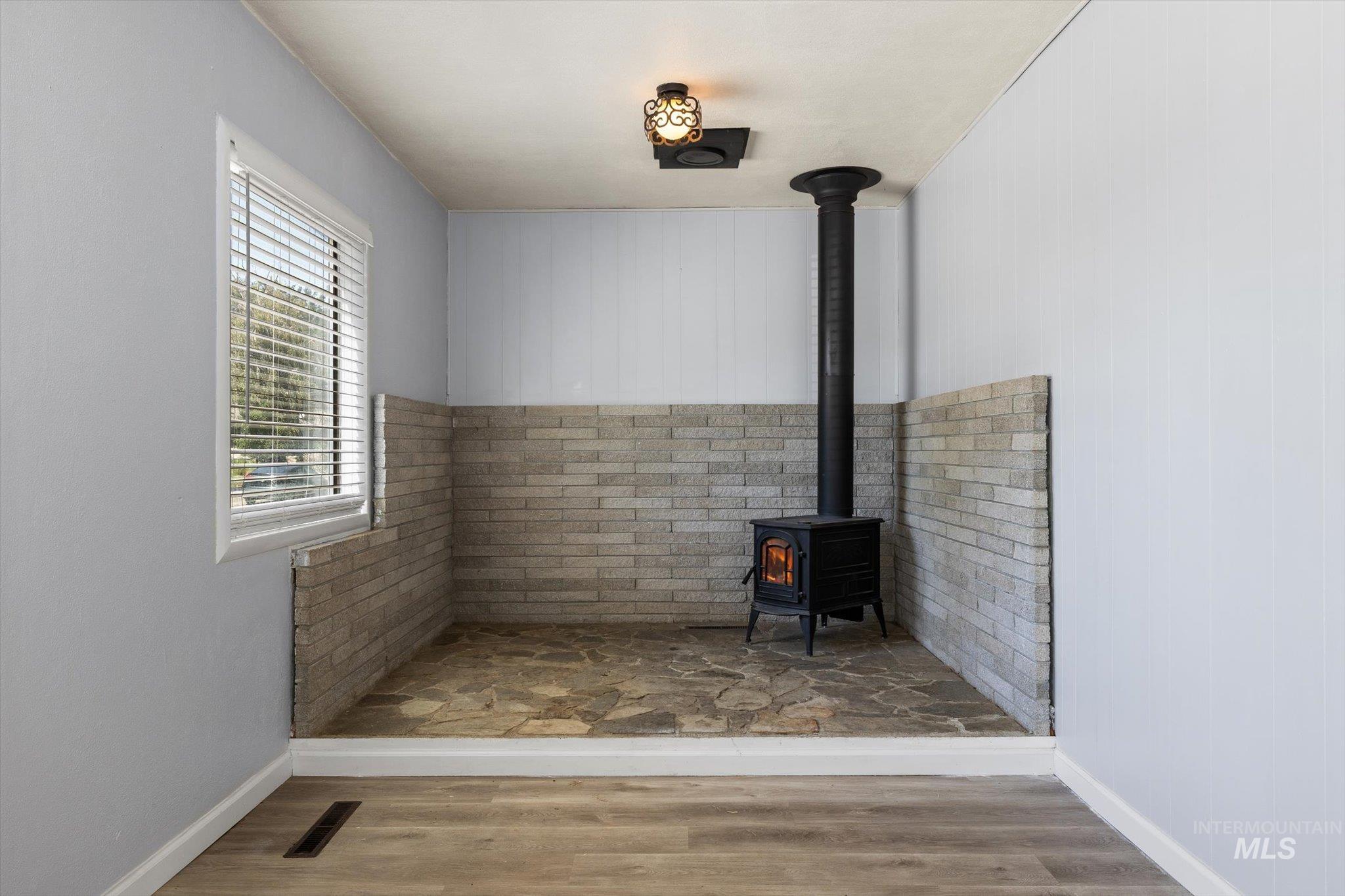 Wood-burning stove with a black metal flue, set within a flagstone-style hearth and surrounded by a light-toned brick wainscoting