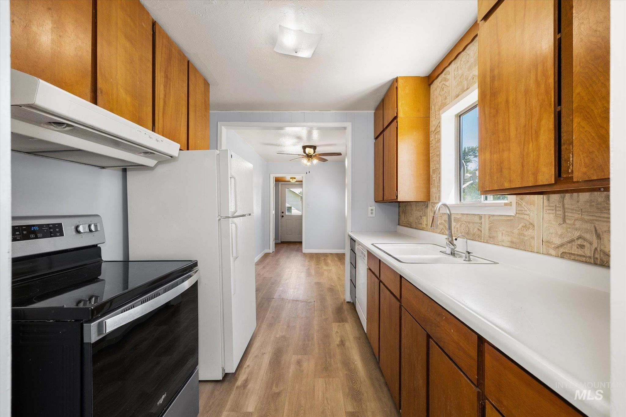 Galley kitchen featuring wood cabinetry, white countertops, and a window above the sink