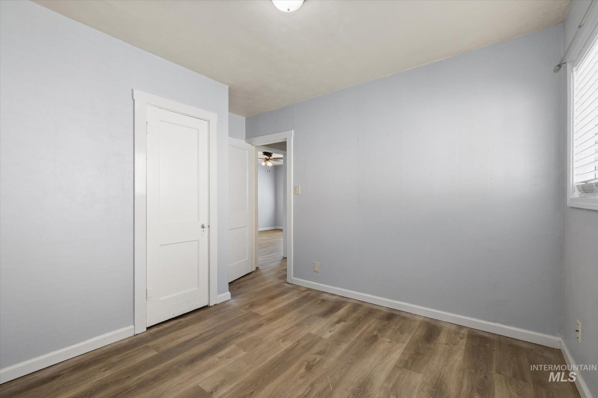 Room featuring wood-finish flooring, light blue wall paint, white trim, and a window with blinds