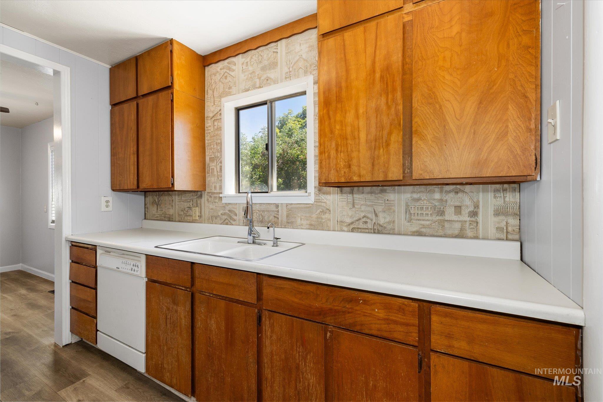 Kitchen featuring wood cabinetry, white countertops, a double-basin sink with a chrome faucet, and a built-in dishwasher