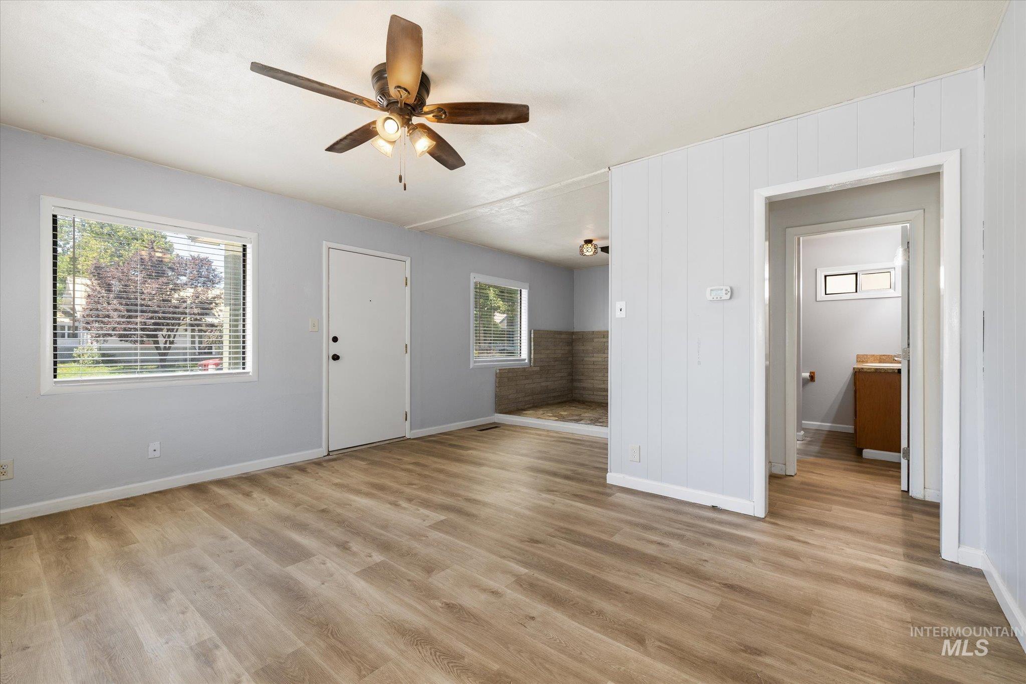 Bright living area featuring wood-finish flooring, light gray walls, and a ceiling fan with integrated lighting
