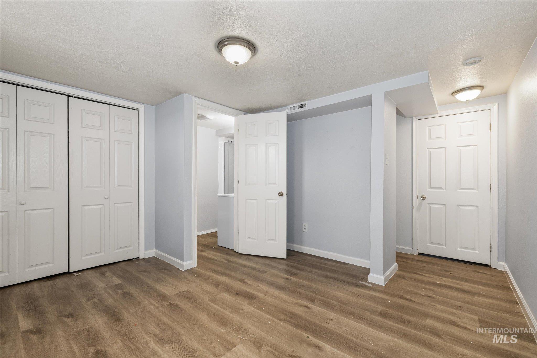 Spacious room featuring wood-finish flooring, light grey walls, and multiple white bi-fold closet doors
