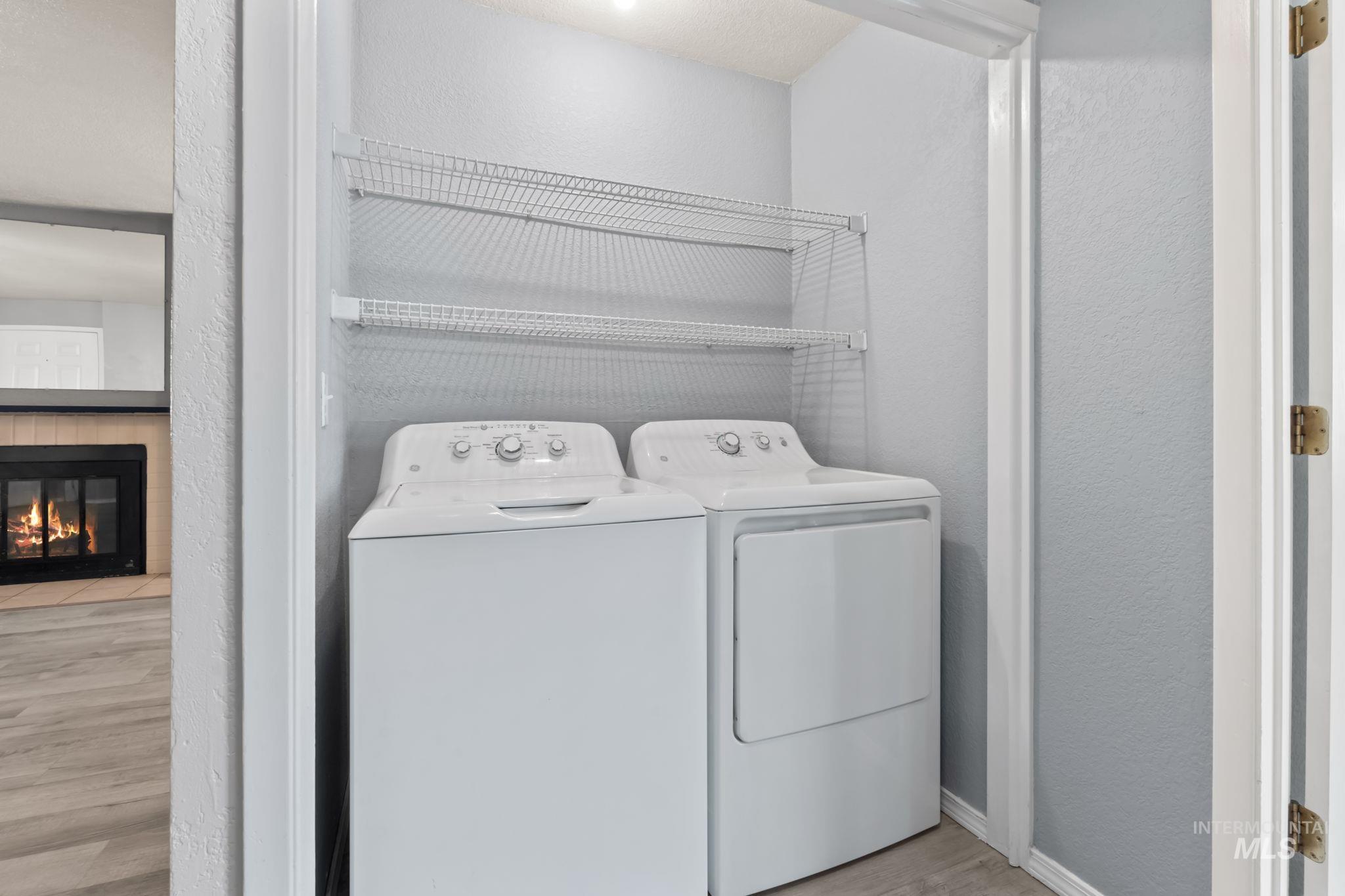 Laundry area featuring a textured wall, light wood finished floors, independent washer and dryer, and a glass covered fireplace