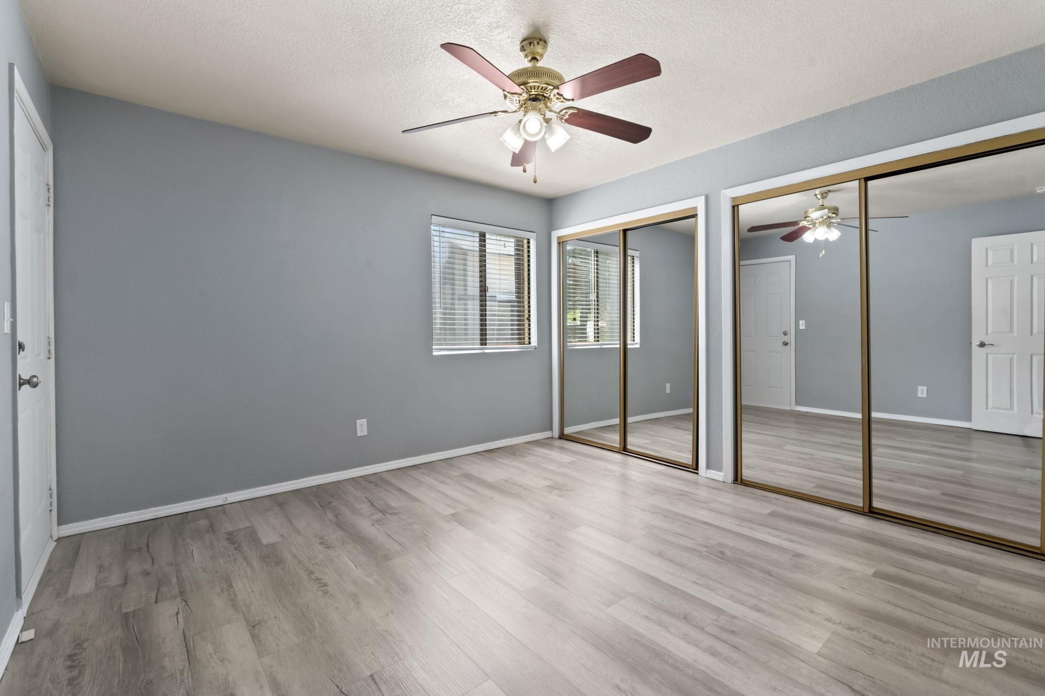 Unfurnished bedroom featuring multiple closets, light wood finished floors, a ceiling fan, and a textured ceiling