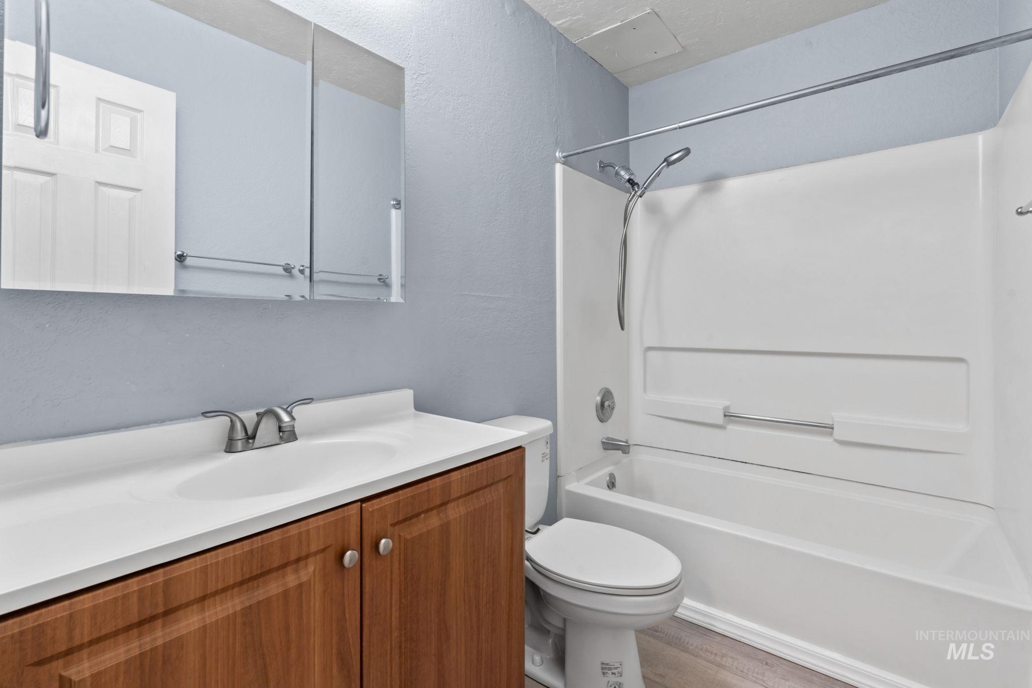 Bathroom with shower / bathtub combination, vanity, a textured wall, and light wood-style floors