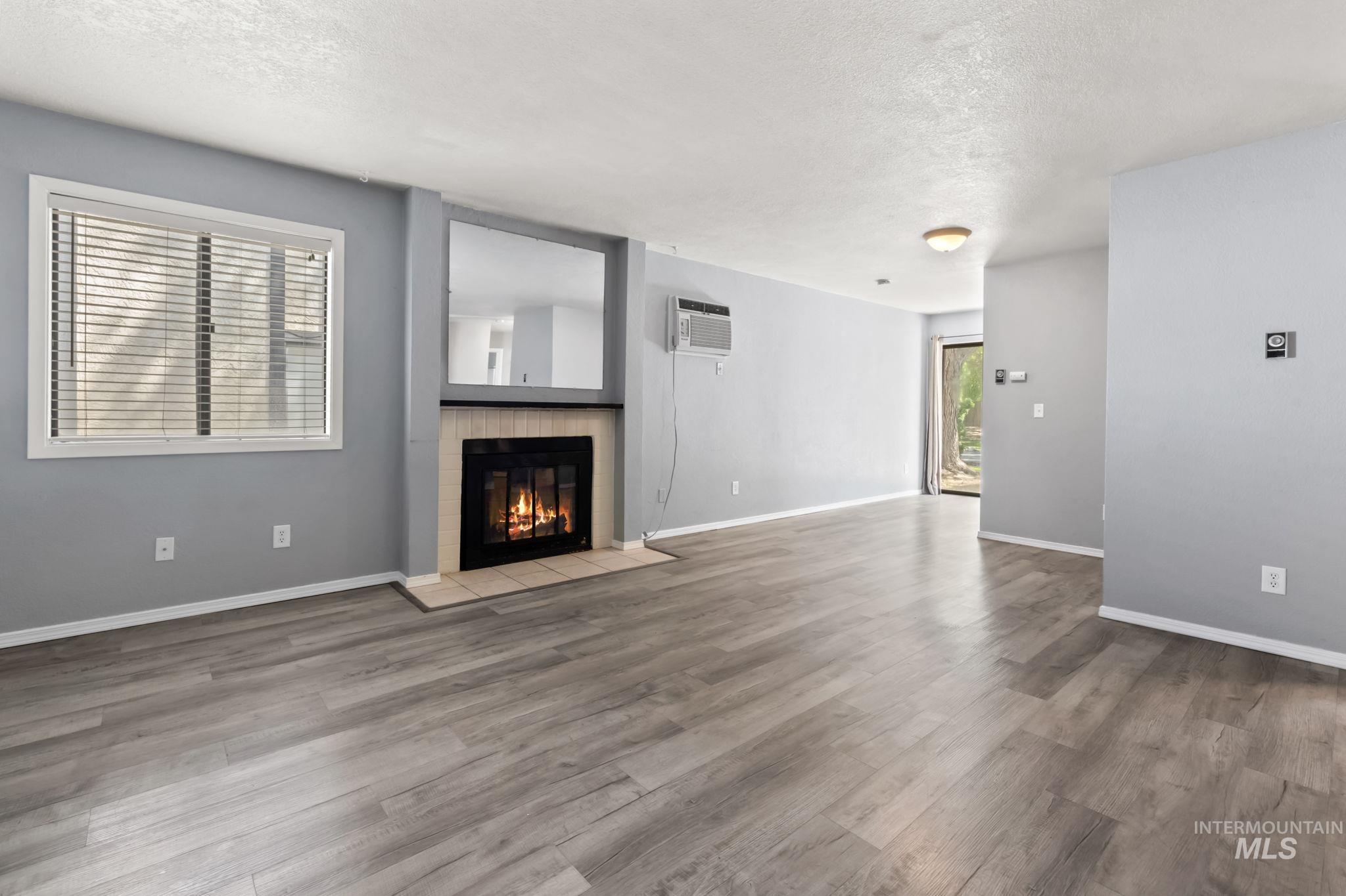 Unfurnished living room featuring a textured ceiling, a glass covered fireplace, light wood-style flooring, and a wall unit AC