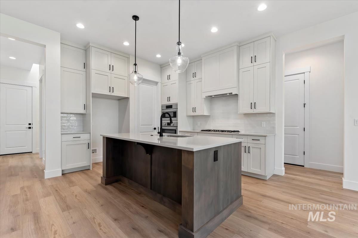 Kitchen with white cabinetry, backsplash, light wood-style floors, a kitchen island with sink, and a kitchen bar