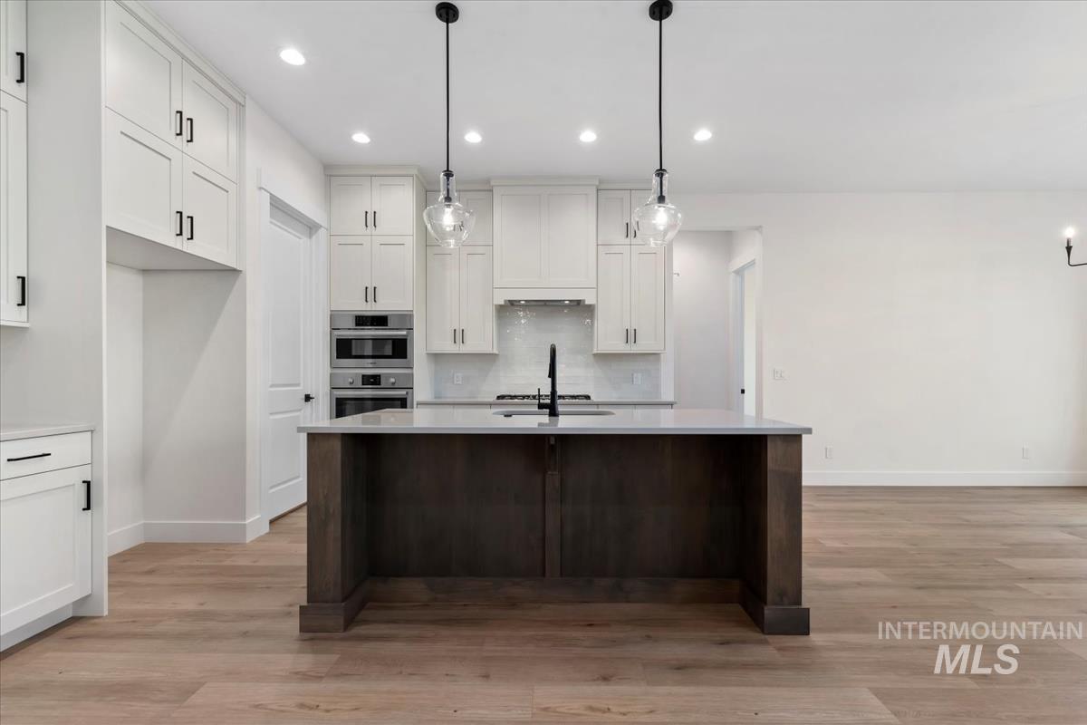 Kitchen featuring white cabinetry, backsplash, a center island with sink, decorative light fixtures, and recessed lighting