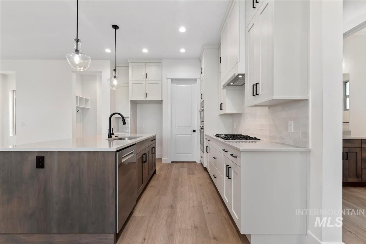 Kitchen with white cabinetry, light wood-type flooring, a center island with sink, pendant lighting, and recessed lighting
