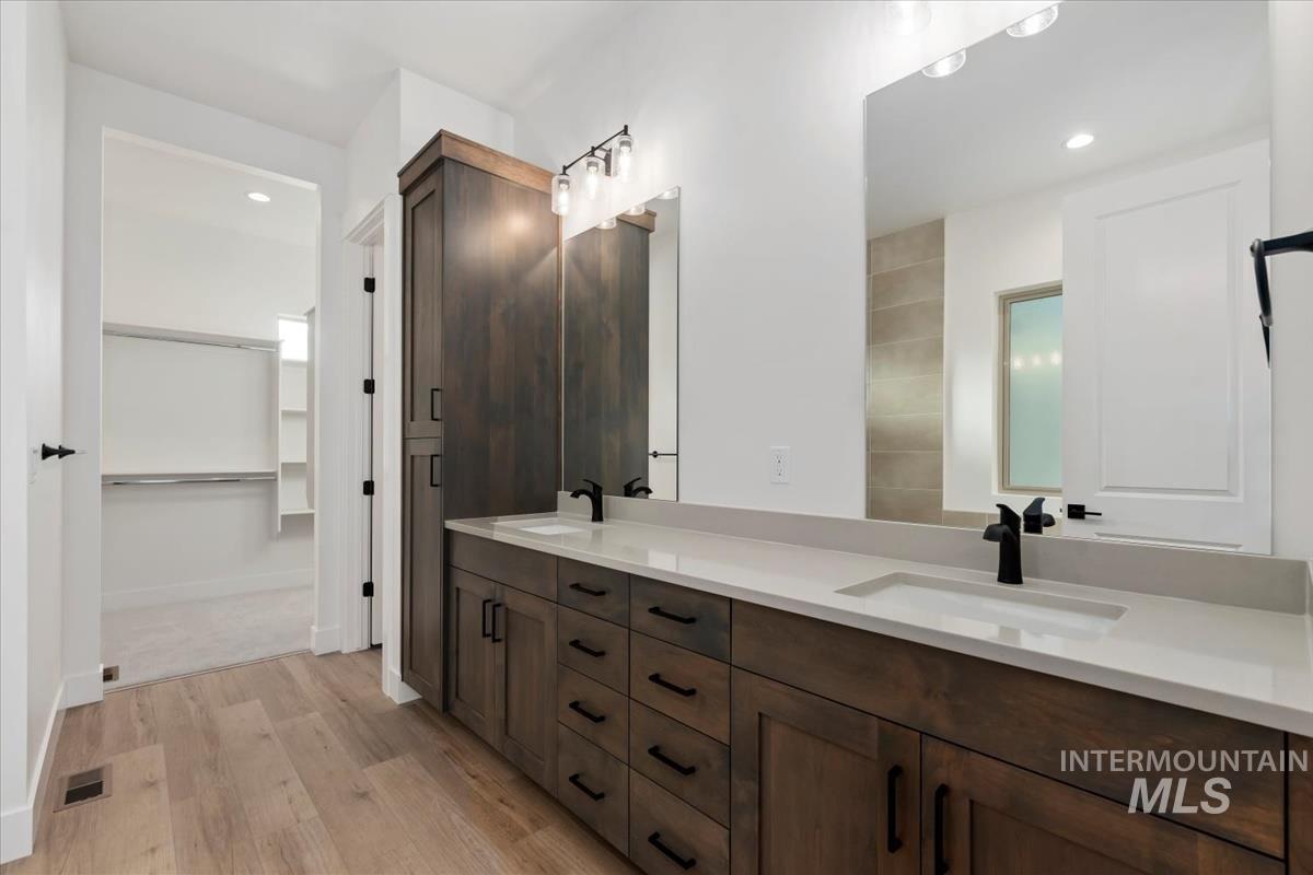 Bathroom with double vanity, light wood finished floors, recessed lighting, and a spacious closet