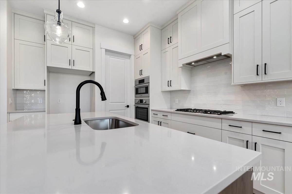 Kitchen featuring pendant lighting, white cabinets, backsplash, light stone counters, and recessed lighting