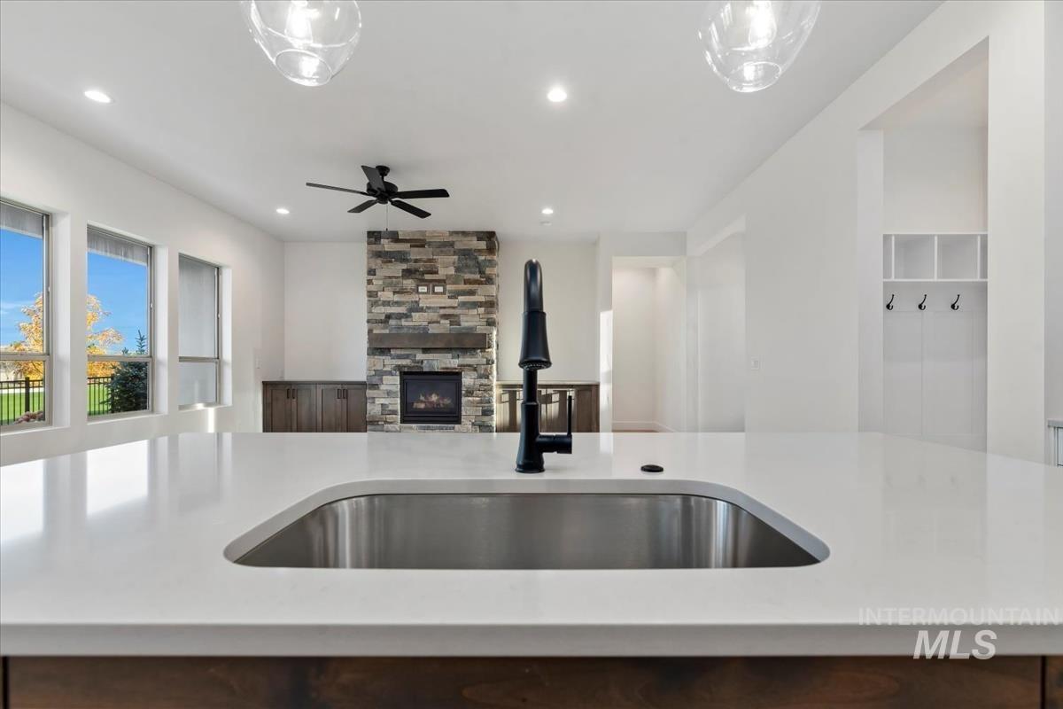 Kitchen featuring a stone fireplace, light stone countertops, recessed lighting, and ceiling fan