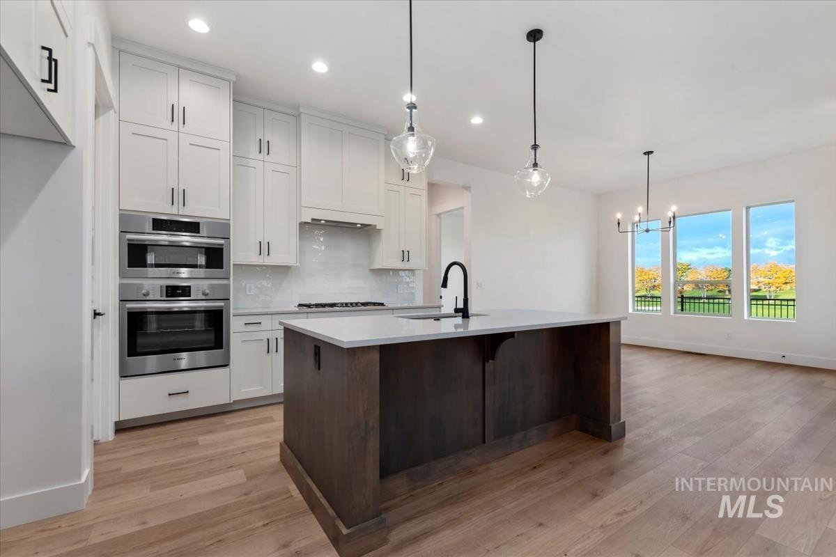 Kitchen with white cabinetry, dark brown cabinetry, decorative backsplash, light wood-type flooring, and a kitchen breakfast bar