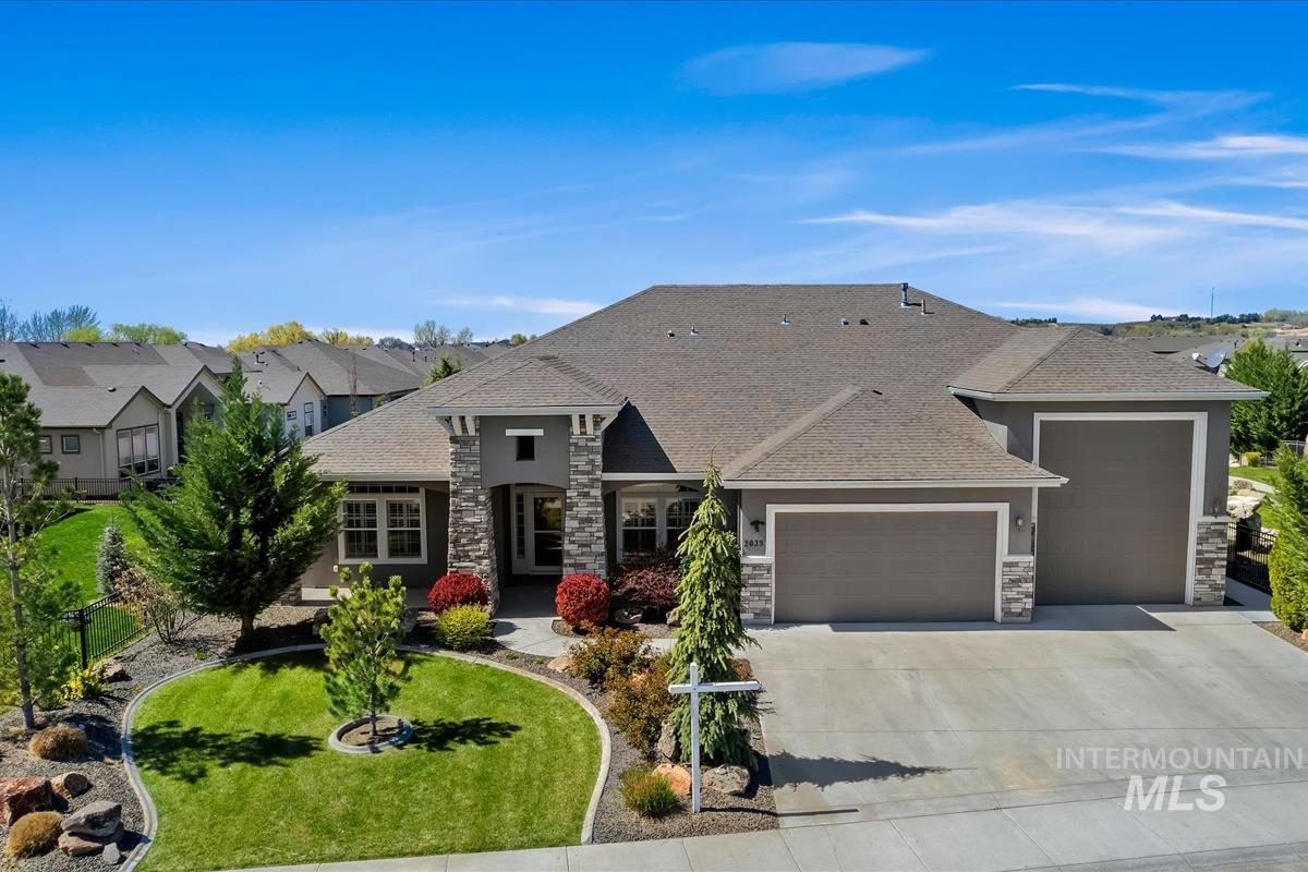 View of front facade with a garage, driveway, a front yard, roof with shingles, and stone siding