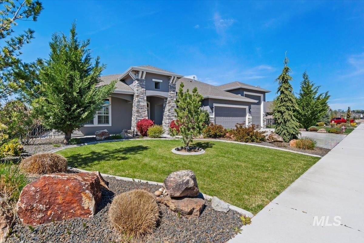 View of front of home featuring stucco siding, an attached garage, a front lawn, and stone siding