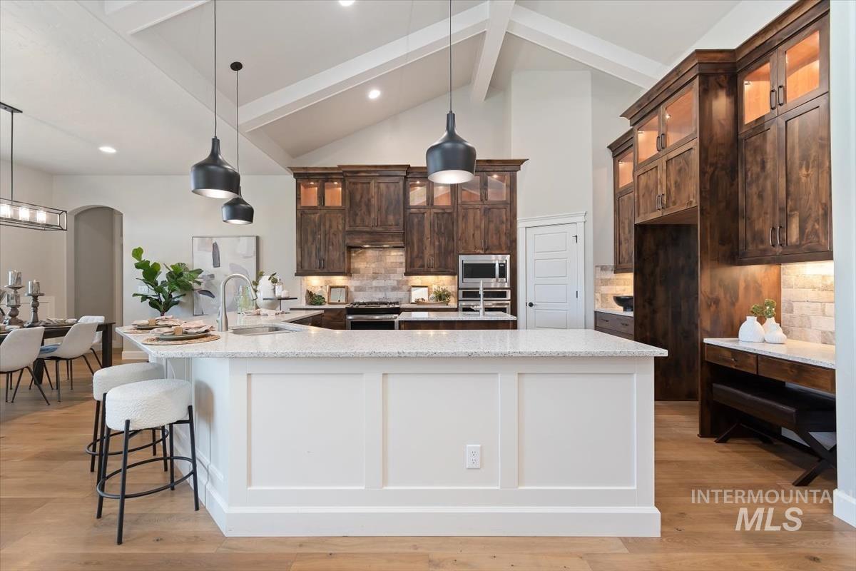 Dual tone kitchen with backsplash, glass fronted cabinets, light stone countertops, light wood finished floors, and arched walkways