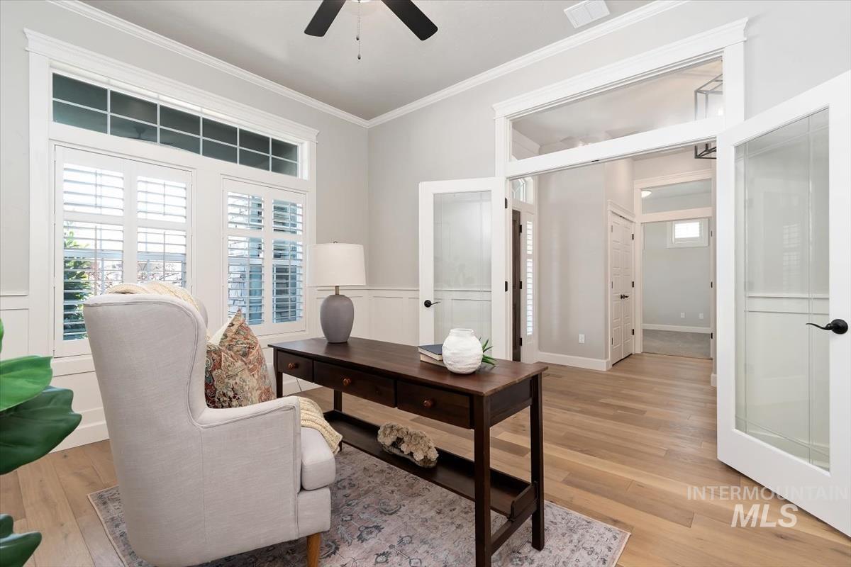 Office area with light wood-style floors, ceiling fan, ornamental molding, a wainscoted wall, and a decorative wall