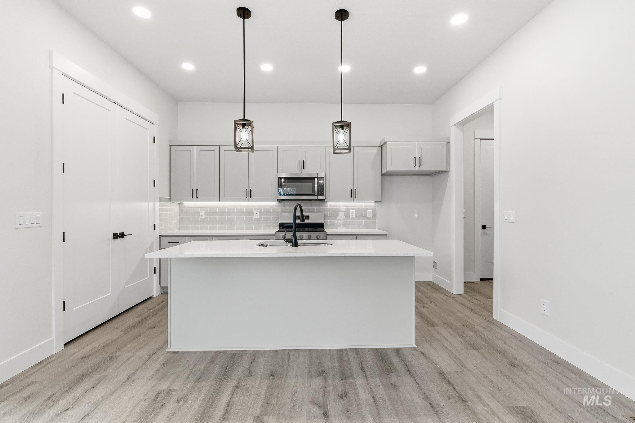Kitchen featuring hanging light fixtures, a kitchen island with sink, light wood-style floors, stainless steel appliances, and backsplash