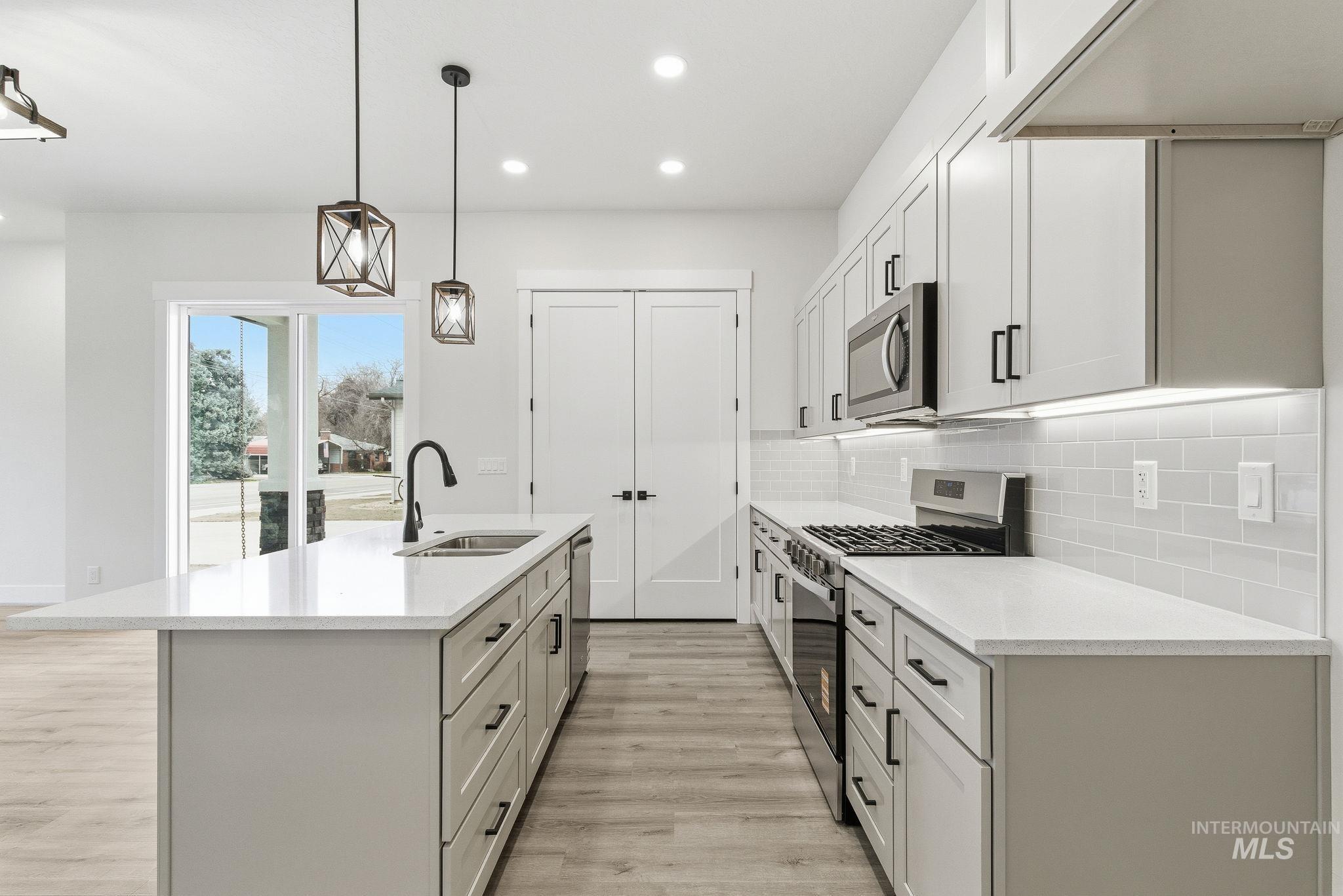 Dual tone kitchen with stainless steel appliances, decorative light fixtures, light stone counters, an island with sink, and light wood-style floors
