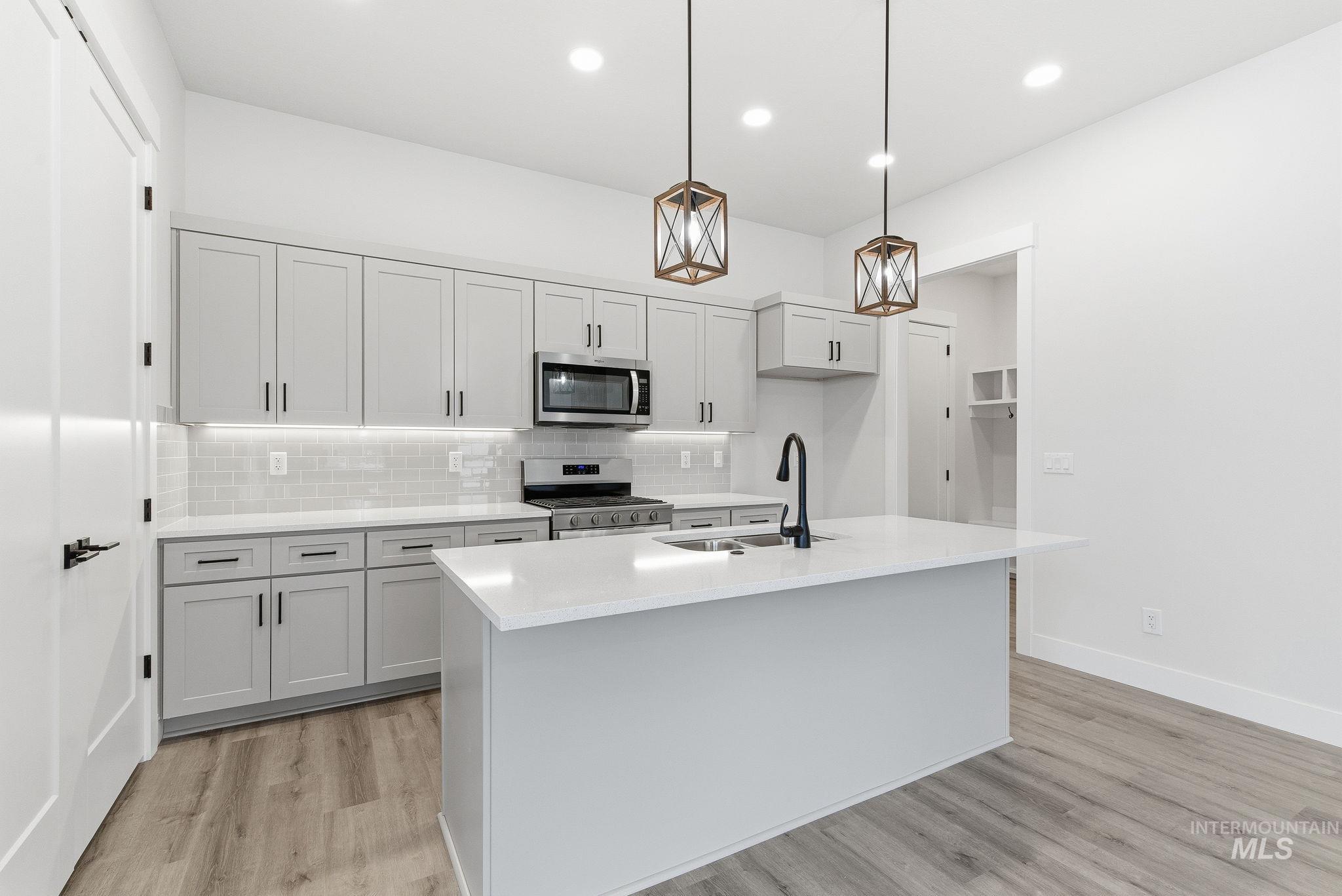 Kitchen with stainless steel appliances, light wood-type flooring, hanging light fixtures, decorative backsplash, and a center island with sink
