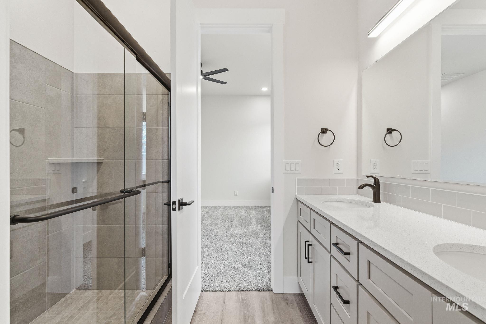 Bathroom with a shower stall, double vanity, light wood finished floors, a ceiling fan, and light carpet