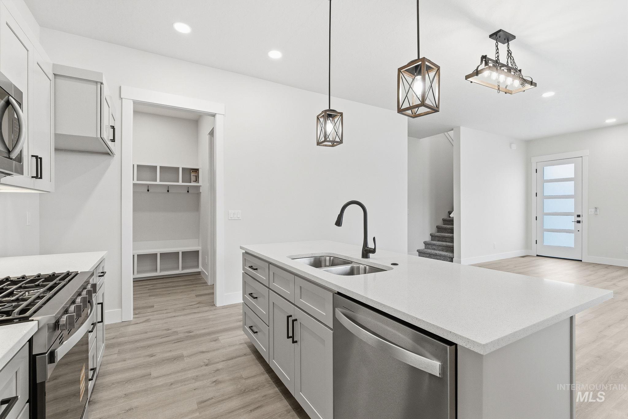 Kitchen with stainless steel appliances, pendant lighting, light wood finished floors, light stone counters, and an island with sink
