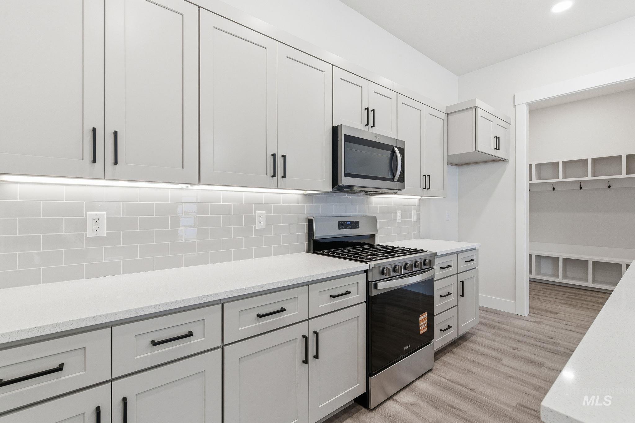 Kitchen featuring stainless steel appliances, light stone countertops, tasteful backsplash, light wood-style flooring, and white cabinets