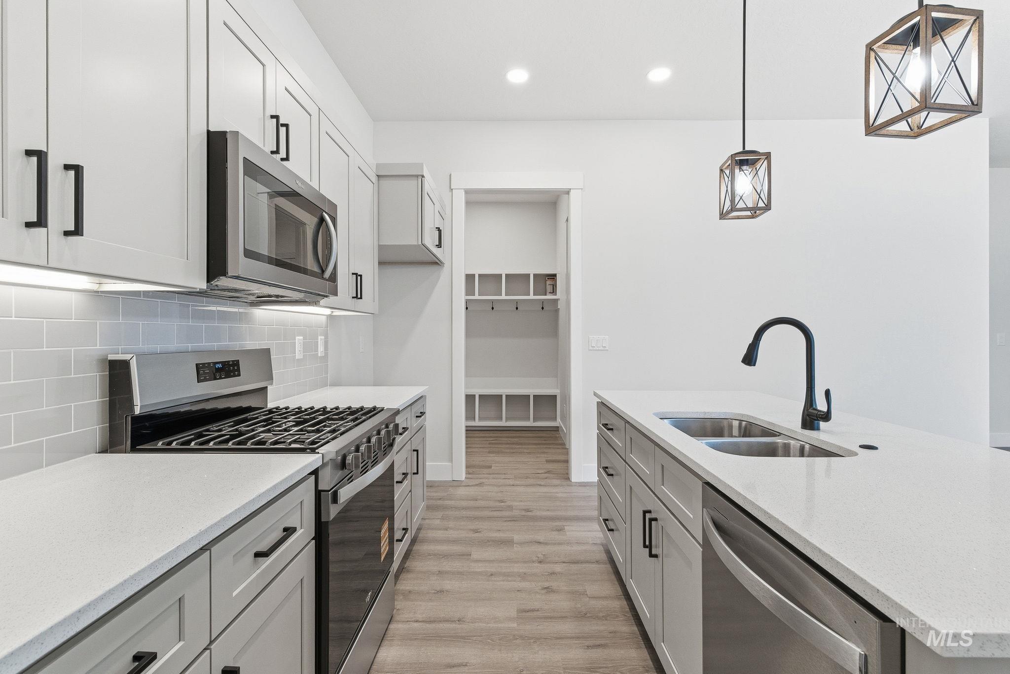 Kitchen with stainless steel appliances, light stone counters, light wood finished floors, pendant lighting, and decorative backsplash