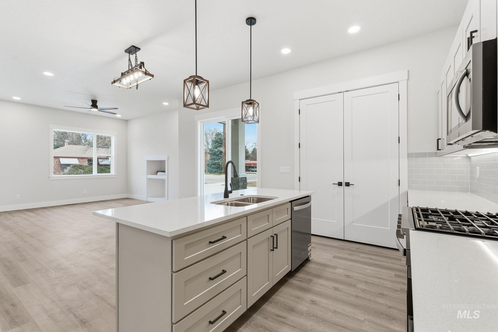 Kitchen with decorative light fixtures, light stone counters, a ceiling fan, a kitchen island with sink, and stainless steel appliances