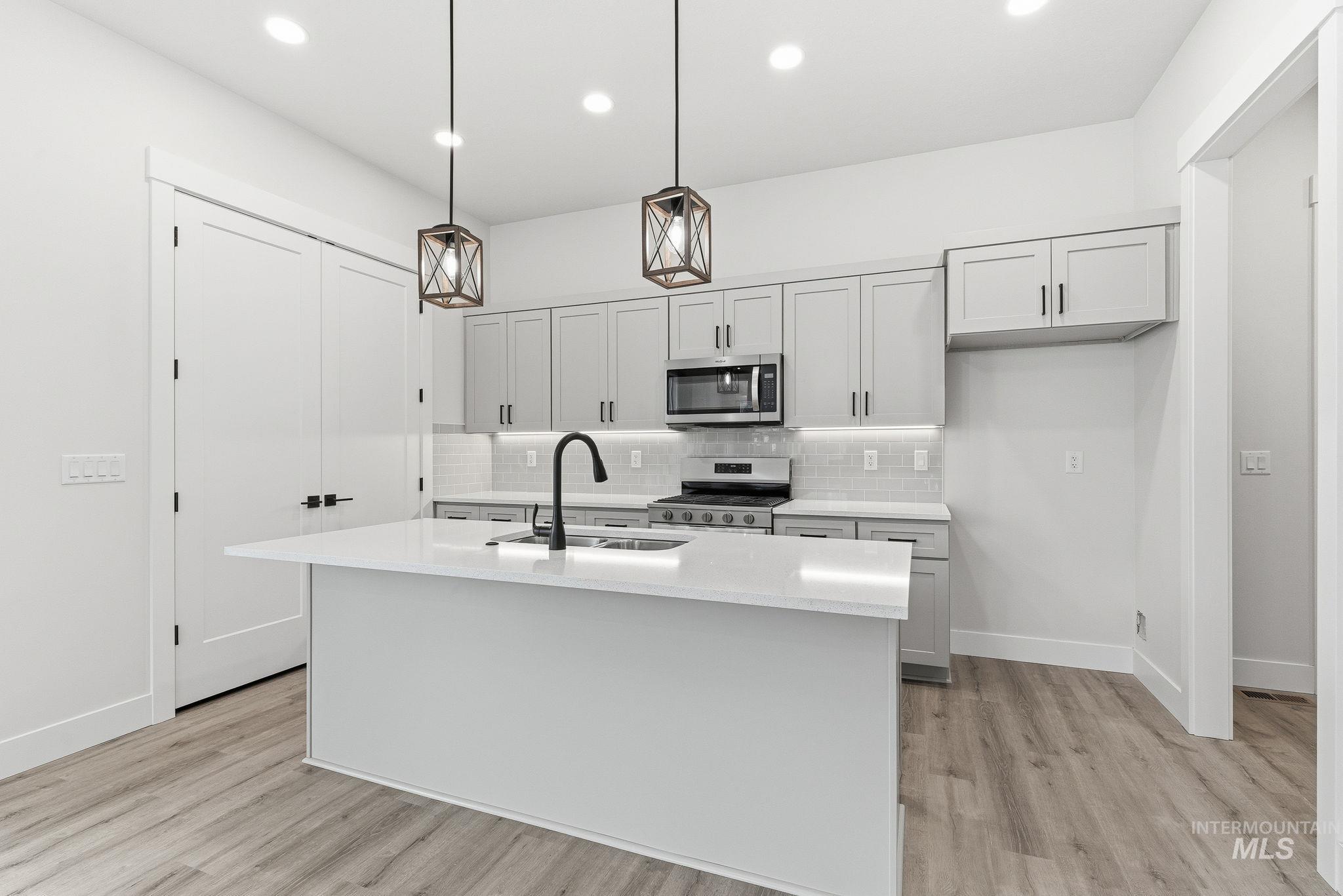 Kitchen with pendant lighting, decorative backsplash, stainless steel appliances, light wood-type flooring, and a center island with sink