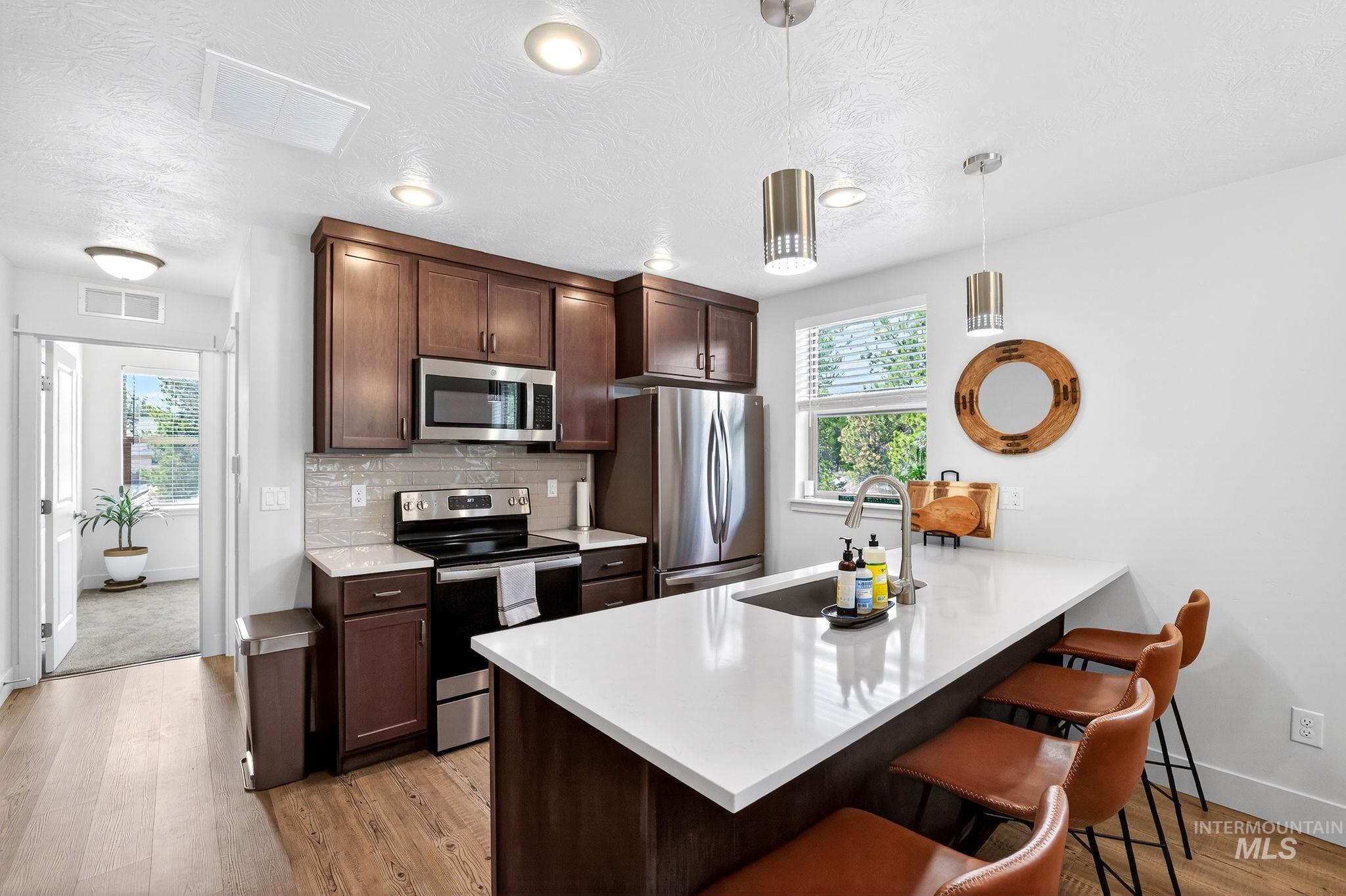 Kitchen featuring wood-finish flooring, dark wood cabinetry, a light-toned countertop, and stainless steel appliances