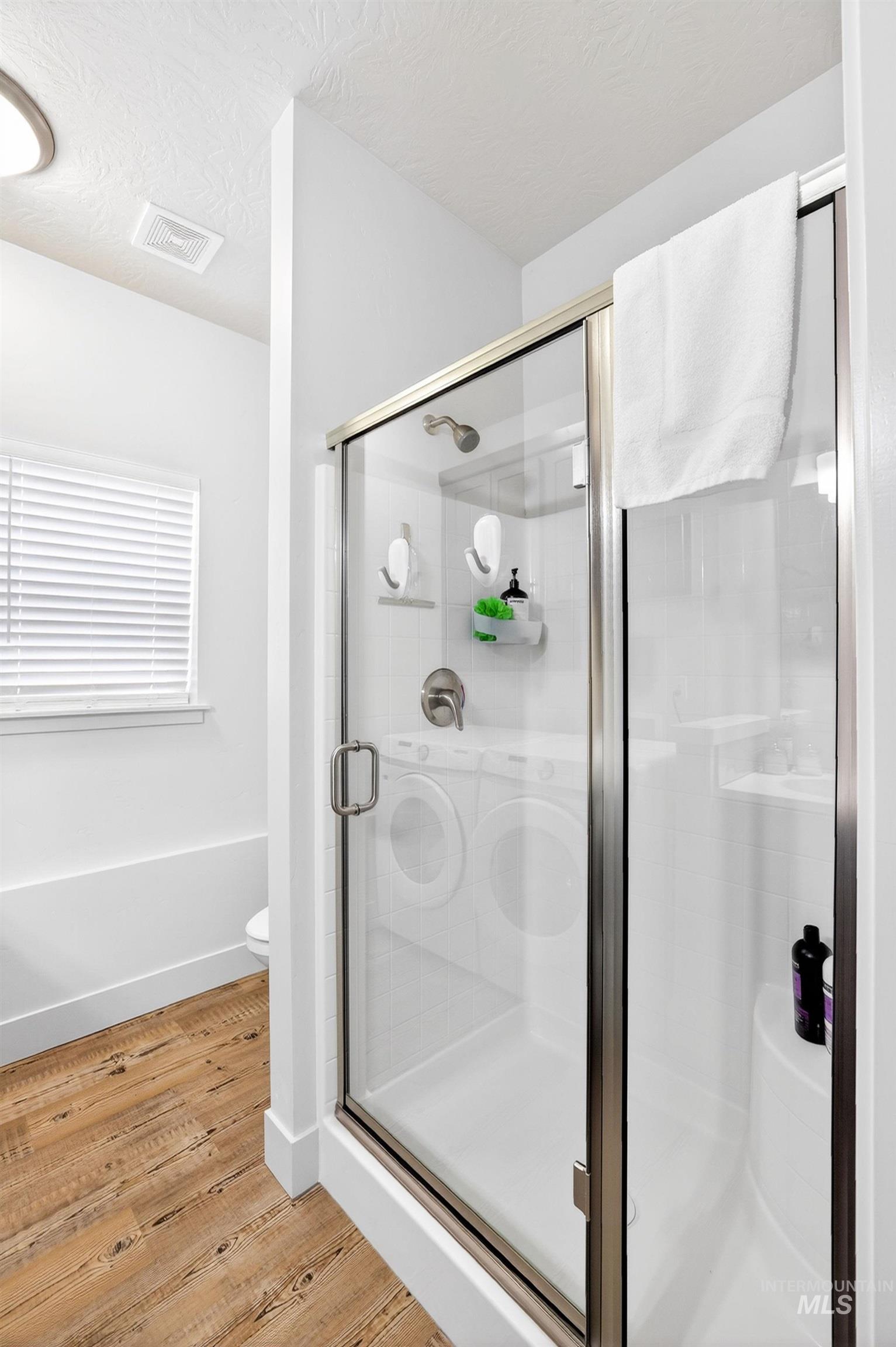 Glass-enclosed shower with brushed nickel hardware, white shower base, and integrated shelving