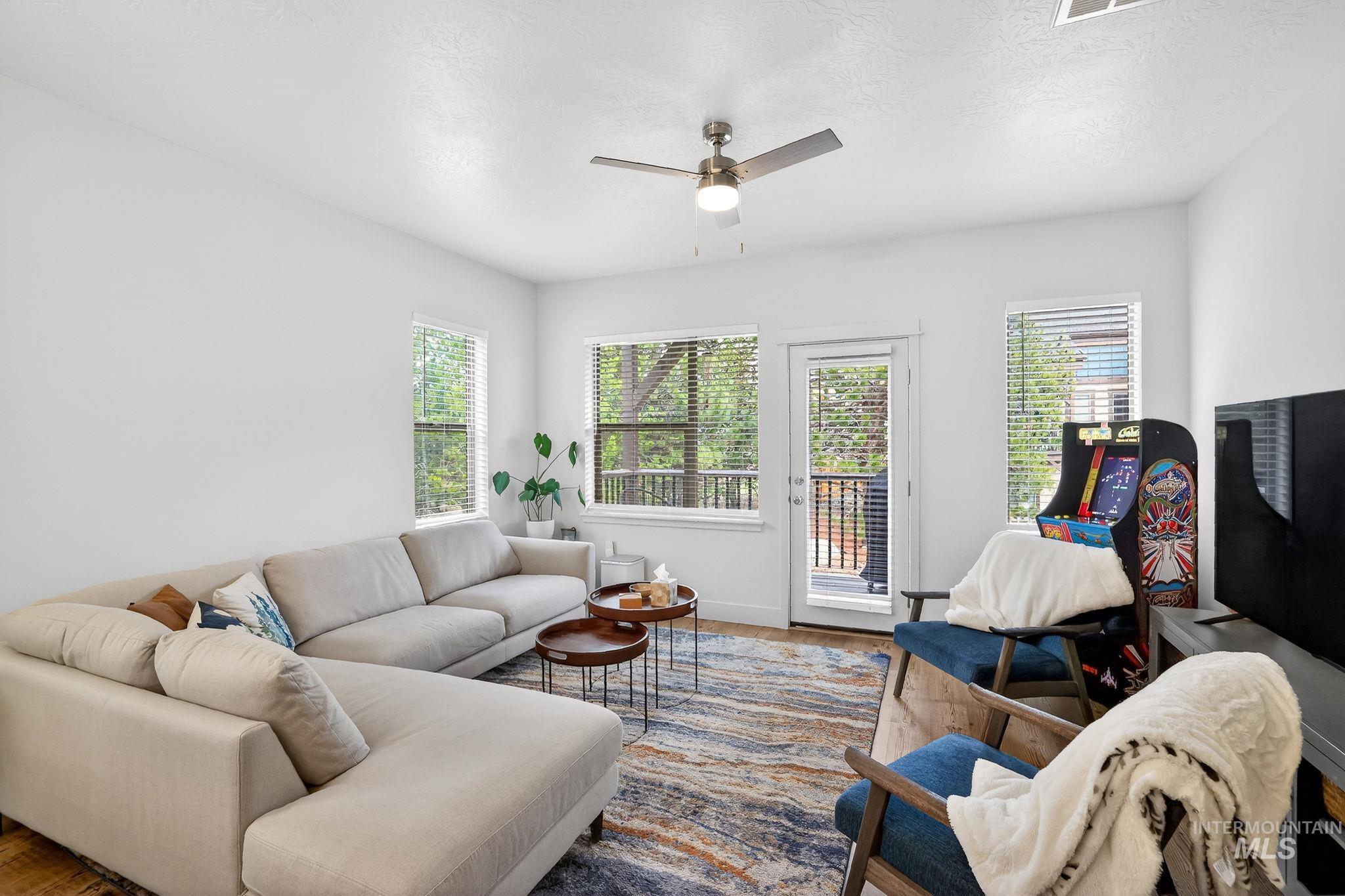 Bright living area with abundant natural light, featuring multiple windows, a ceiling fan with integrated lighting, and a glass-paned door leading to an outdoor space