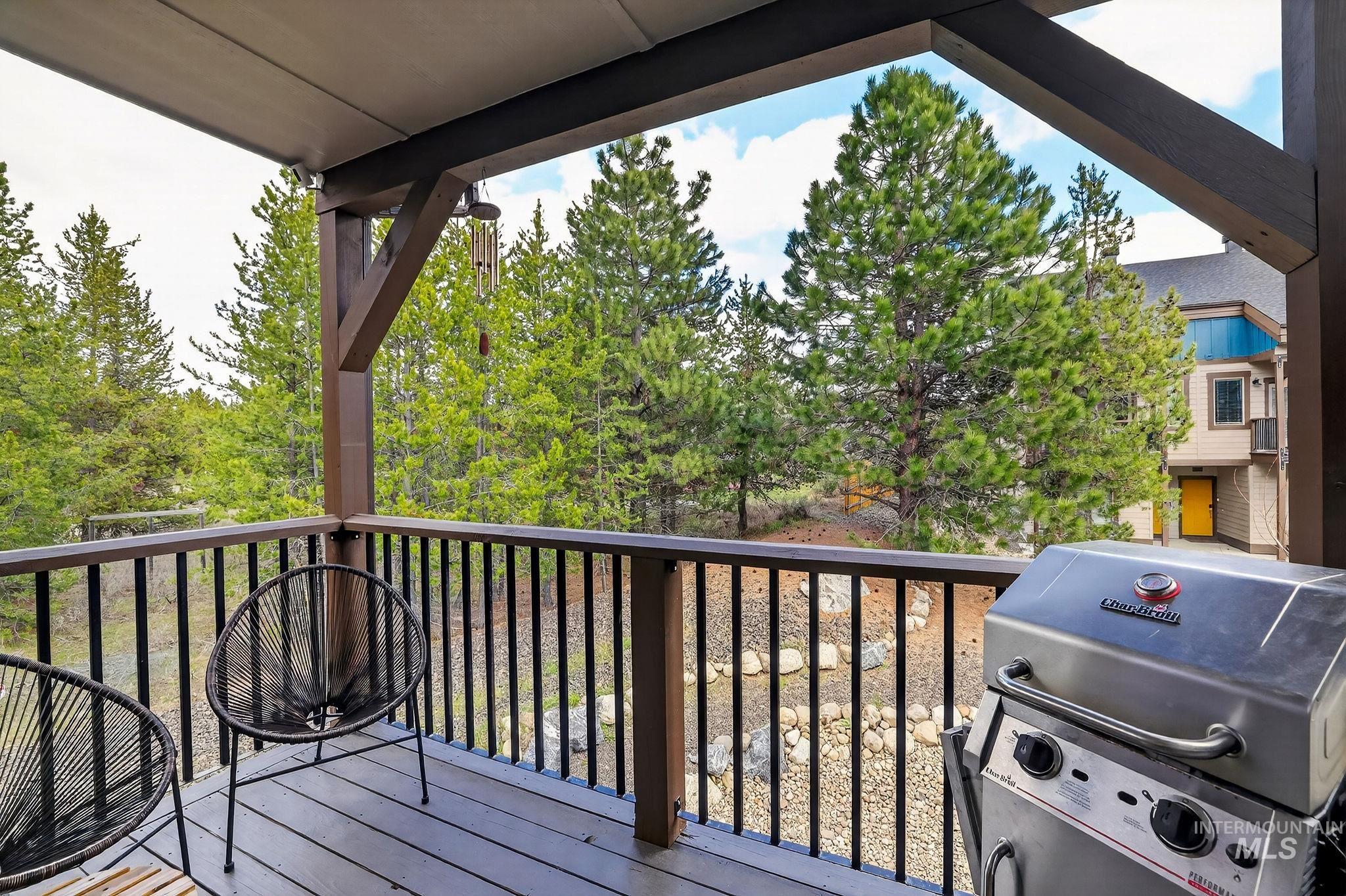Covered outdoor deck with wood-finish flooring, dark wood railing, and surrounding evergreen trees